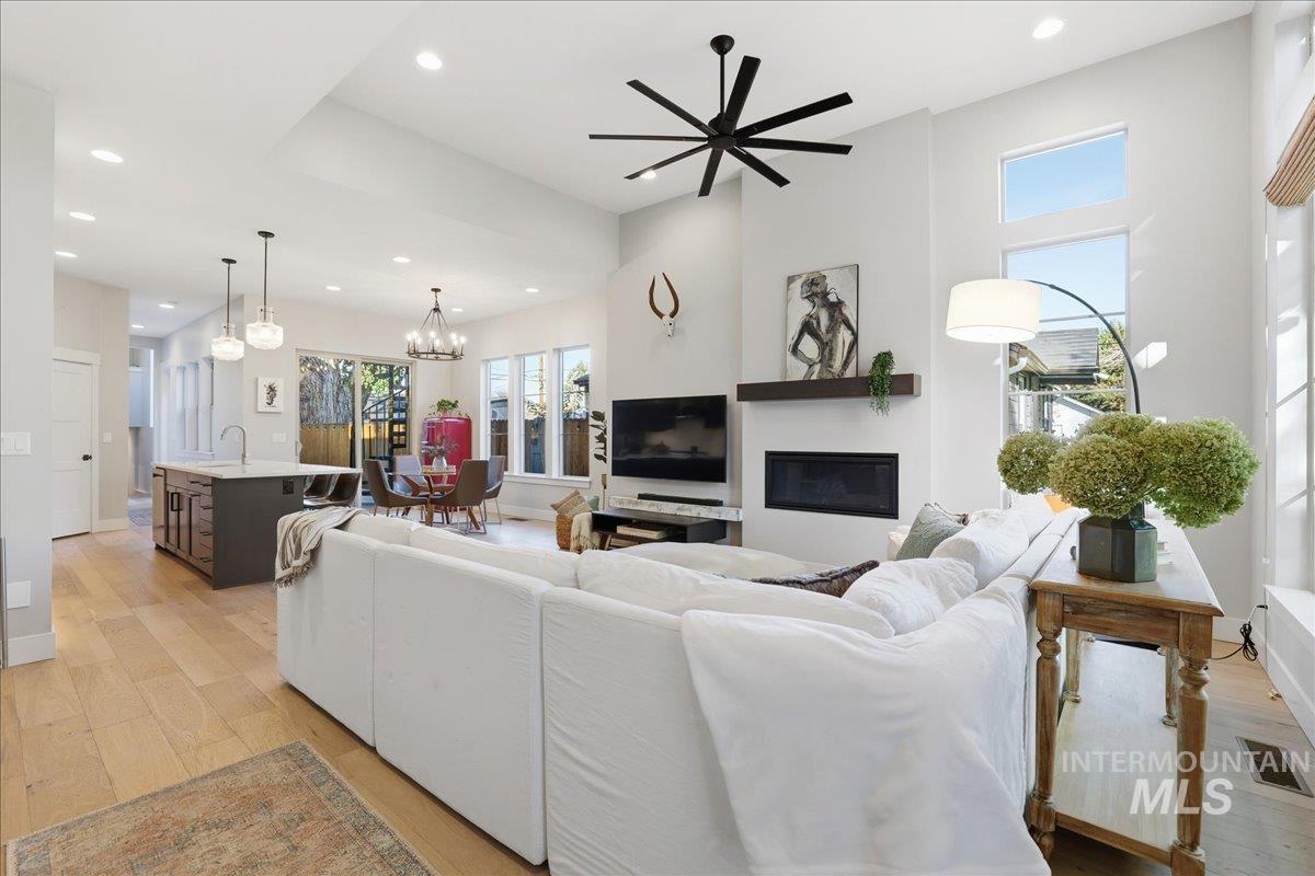 Living room featuring a glass covered fireplace, light wood finished floors, recessed lighting, a ceiling fan, and a chandelier