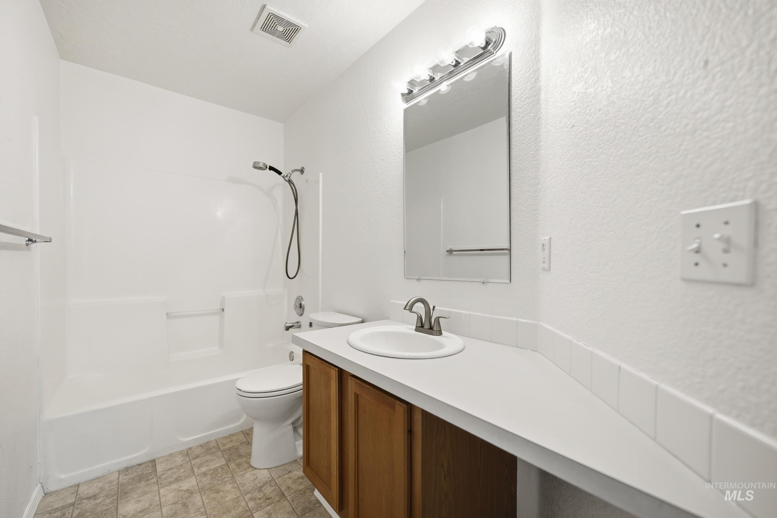 Full bath with vanity, a textured wall, and washtub / shower combination