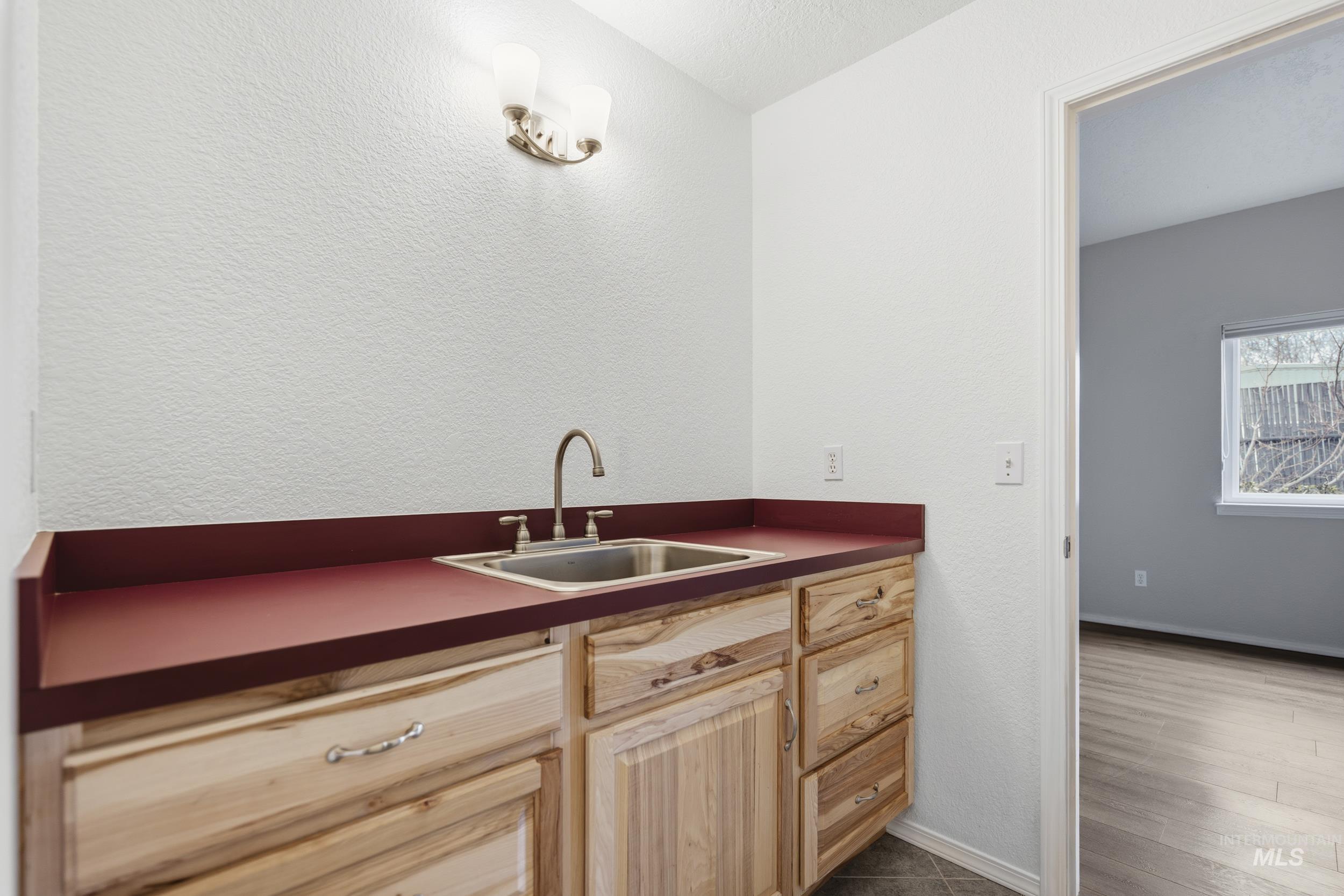 Bar area with light wood finish cabinets, dark countertops, a textured wall, and dark wood finished floors