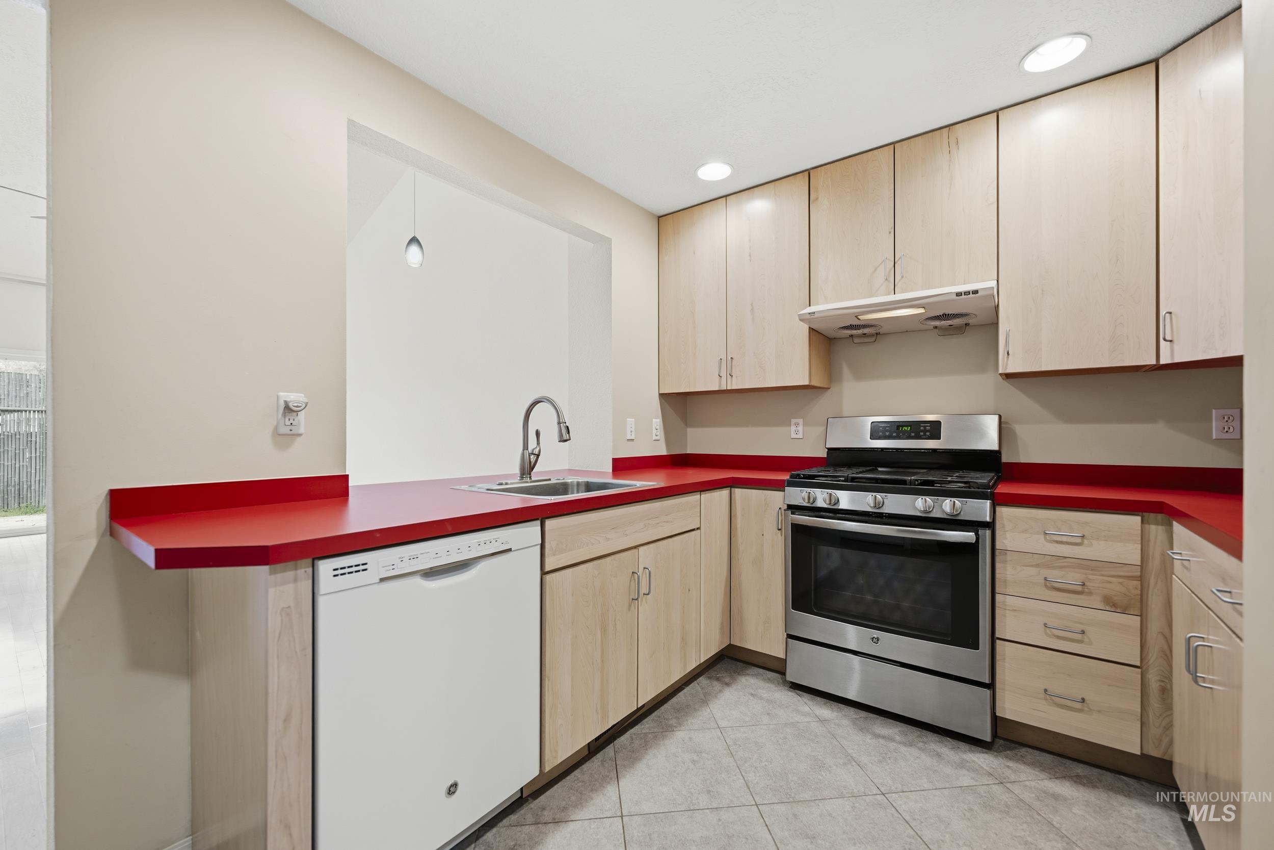 Kitchen featuring light wood finish cabinets, stainless steel gas range oven, white dishwasher, dark countertops, and recessed lighting