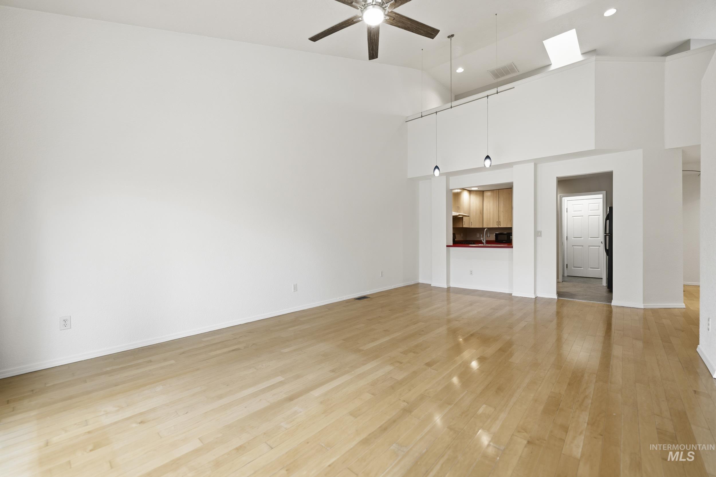 Unfurnished living room featuring ceiling fan, light wood-style flooring, and lofted ceiling