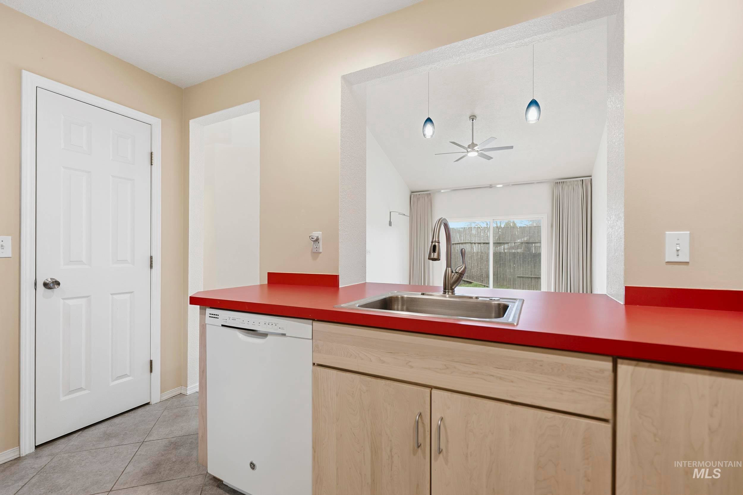 Kitchen with light wood finish cabinetry, dishwasher, lofted ceiling, light tile patterned floors, and a ceiling fan