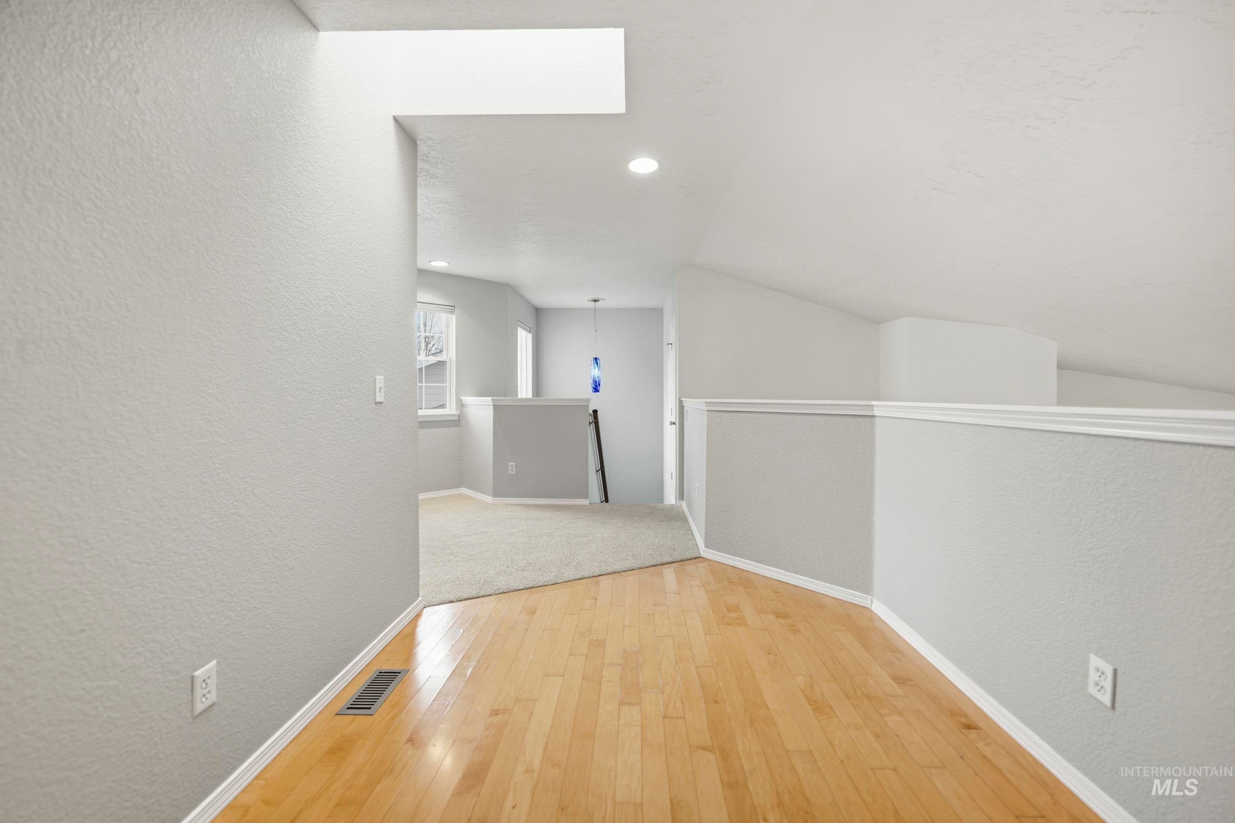 Corridor with a textured wall, light wood-style flooring, lofted ceiling, and recessed lighting