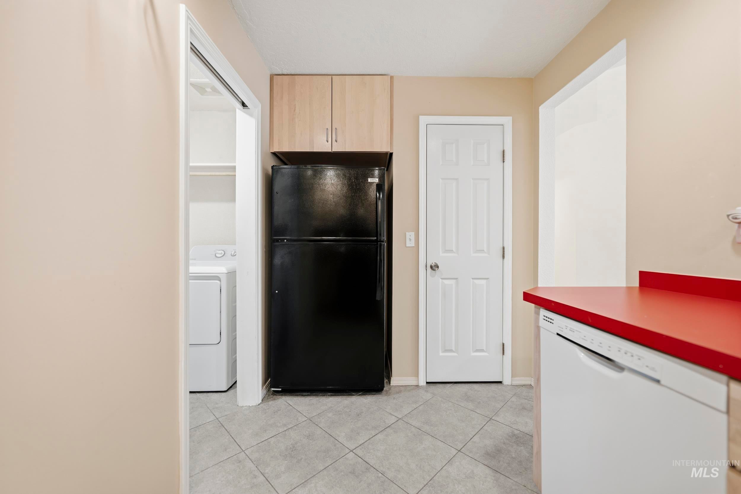 Kitchen featuring freestanding refrigerator, dishwasher, washer / dryer, light tile patterned flooring, and light wood finish cabinets