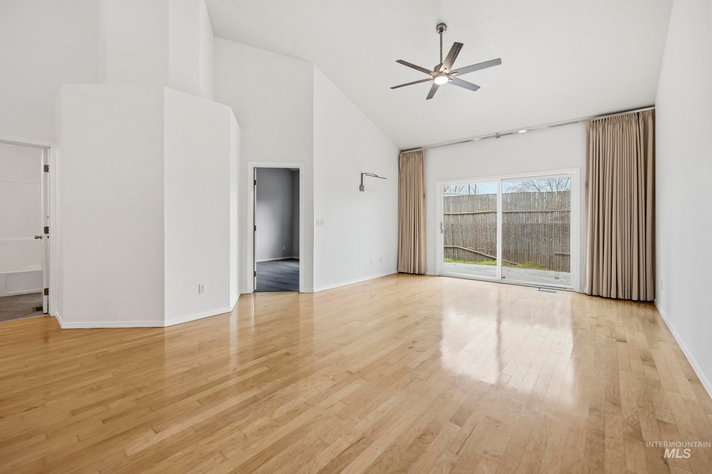 Unfurnished living room with a ceiling fan, light wood finished floors, and vaulted ceiling