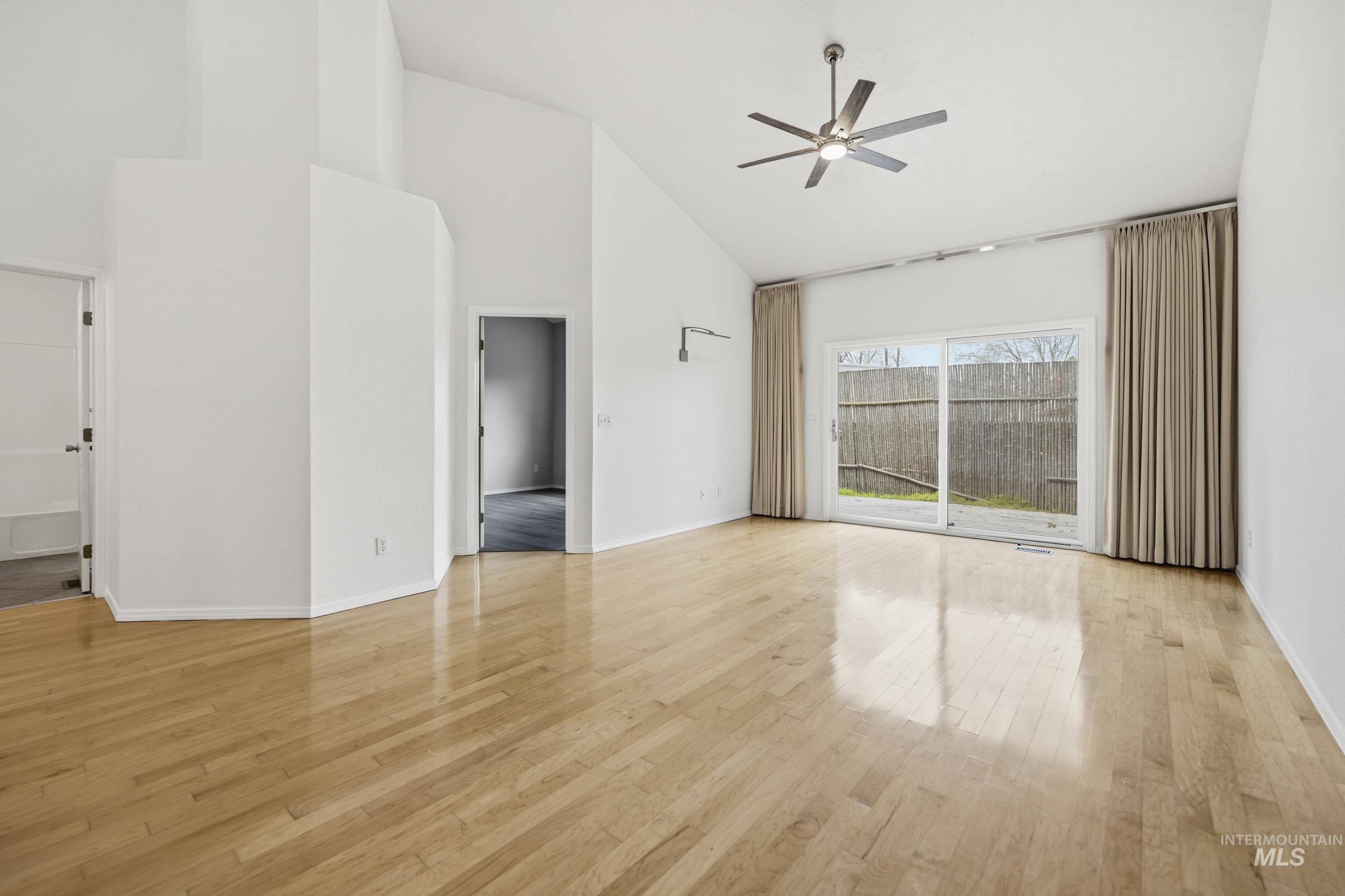 Unfurnished living room with a ceiling fan, light wood finished floors, and vaulted ceiling