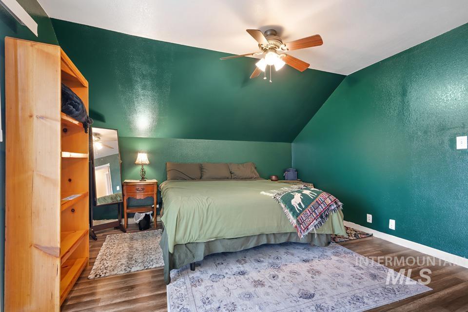 Bedroom featuring a textured wall, wood finished floors, vaulted ceiling, and ceiling fan