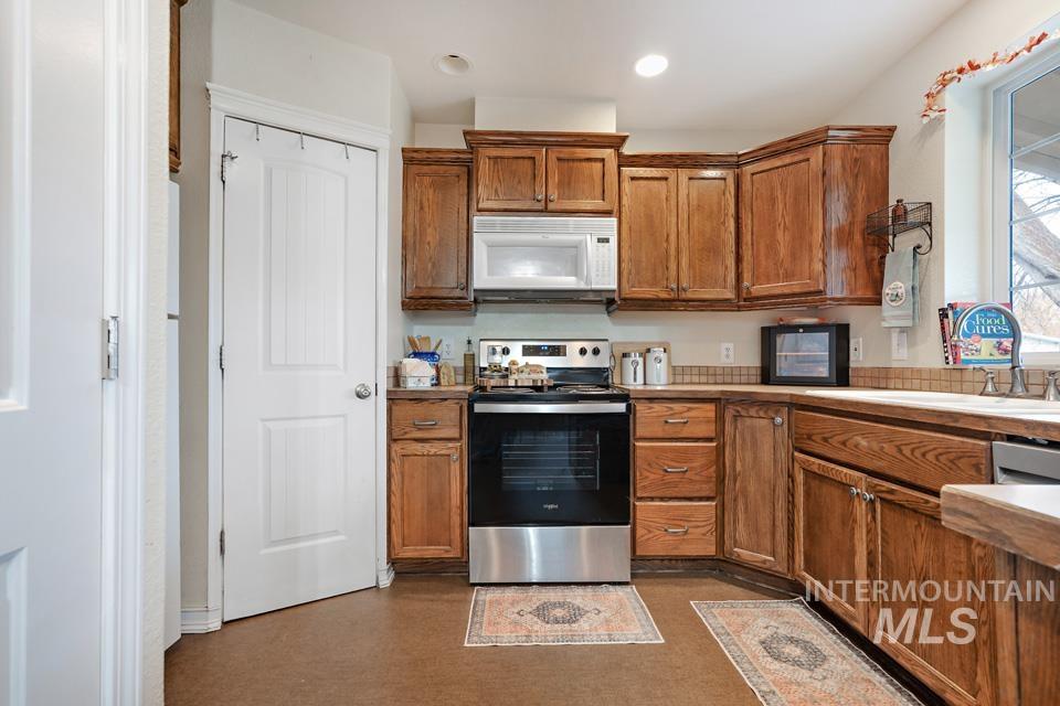 Kitchen featuring stainless steel range with electric stovetop, brown cabinets, white microwave, recessed lighting, and light countertops
