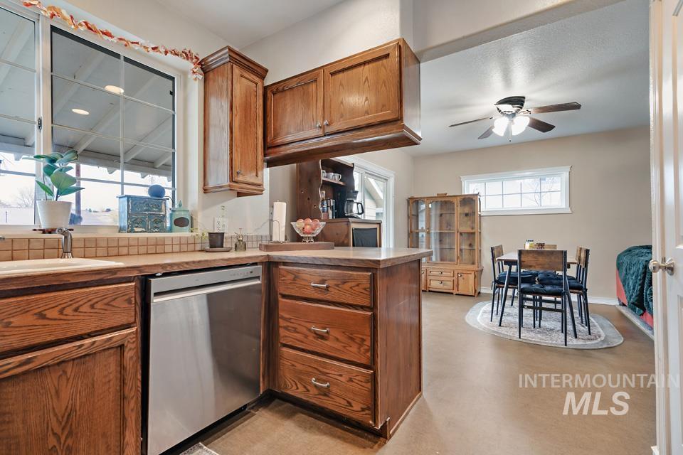 Kitchen featuring stainless steel dishwasher, brown cabinetry, a peninsula, finished concrete floors, and light countertops