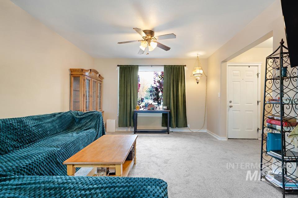 Carpeted living area featuring a ceiling fan and baseboards