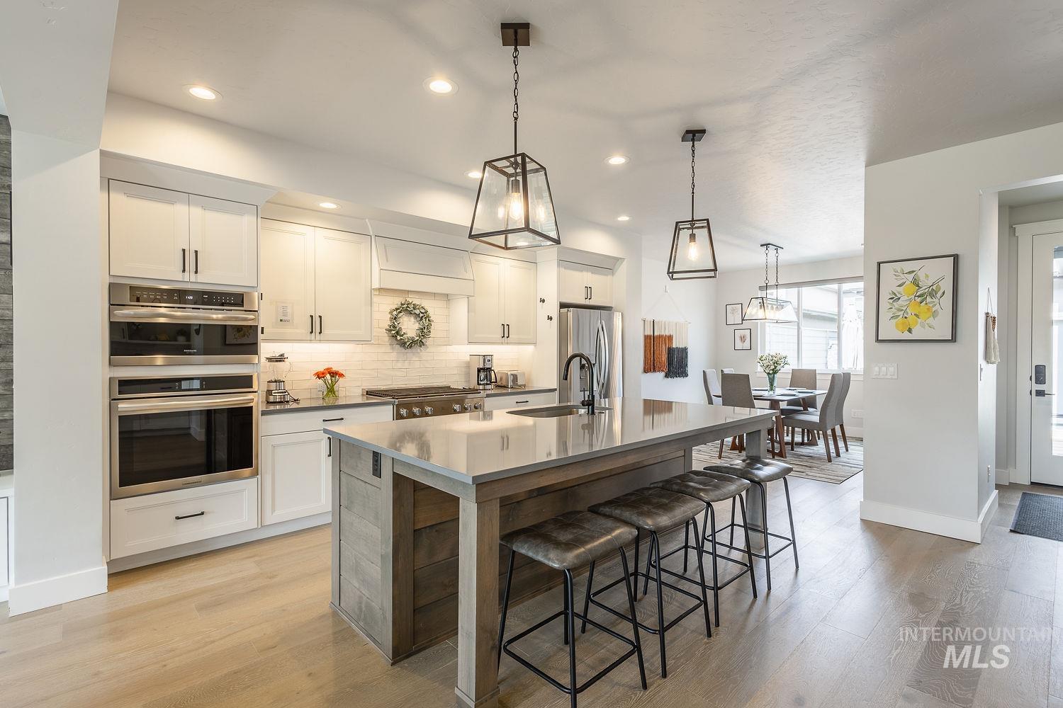 Kitchen with backsplash, white cabinets, pendant lighting, stainless steel appliances, and light wood-style flooring