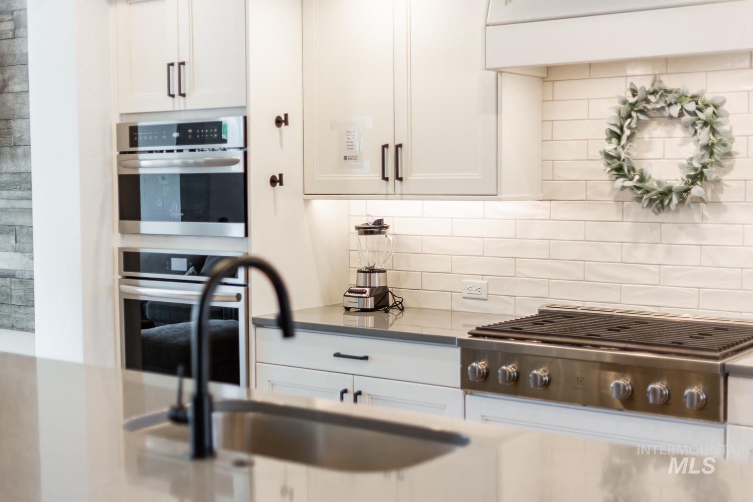 Kitchen featuring white cabinets, backsplash, appliances with stainless steel finishes, and light stone countertops