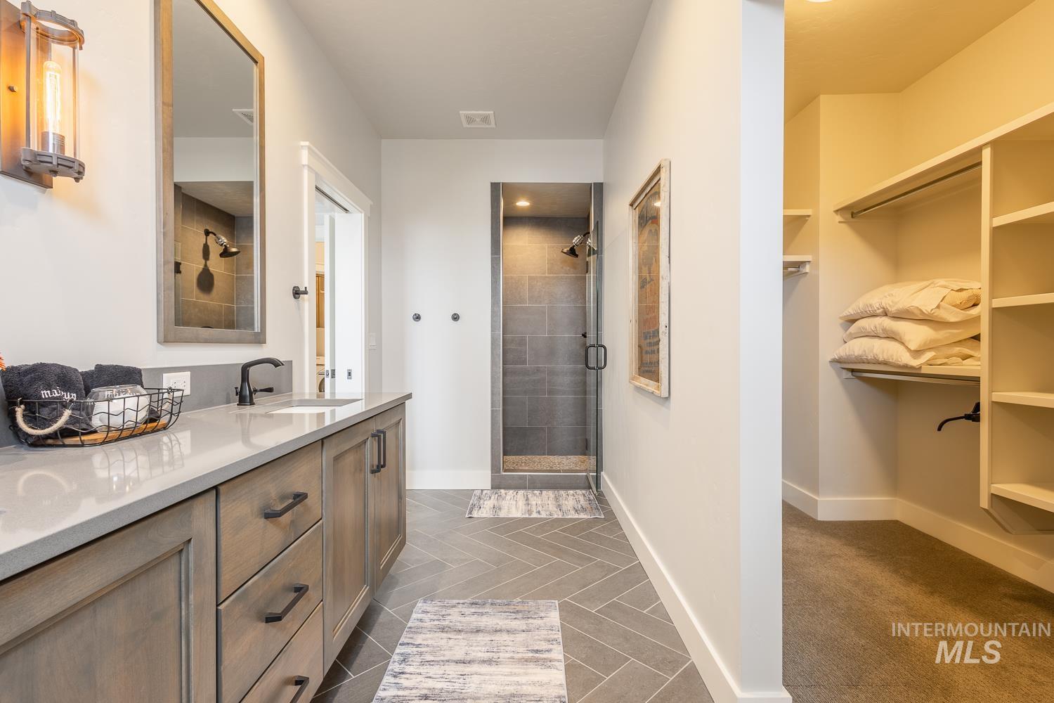 Full bath with double vanity, a shower stall, and a spacious closet