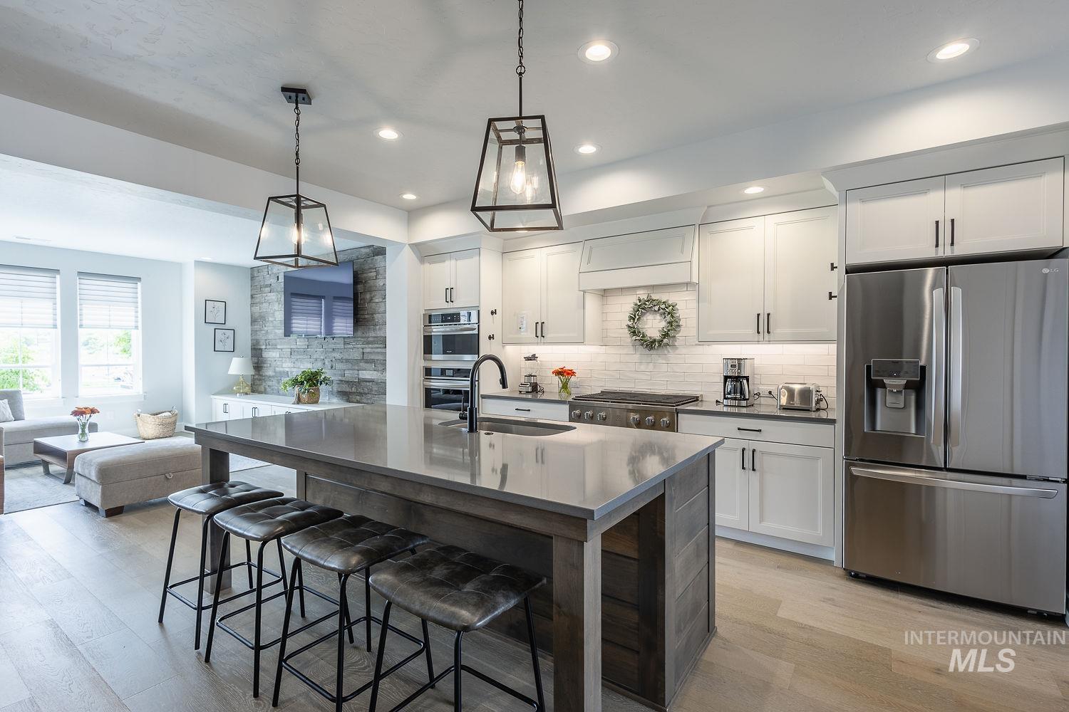 Kitchen featuring appliances with stainless steel finishes, white cabinetry, decorative backsplash, a breakfast bar area, and decorative light fixtures