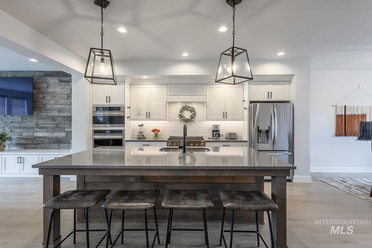 Kitchen featuring tasteful backsplash, white cabinets, appliances with stainless steel finishes, recessed lighting, and decorative light fixtures