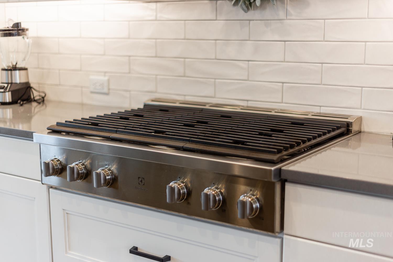 Kitchen view of stainless steel gas stovetop, white cabinetry, dark stone counters, and backsplash