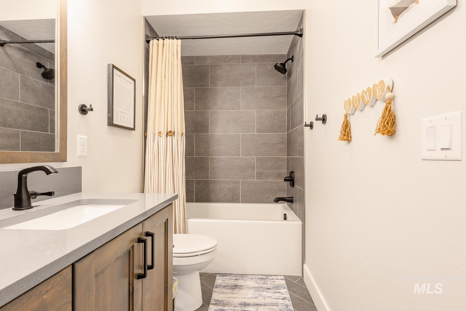 Full bath with vanity, shower / bath combo with shower curtain, and dark tile patterned flooring