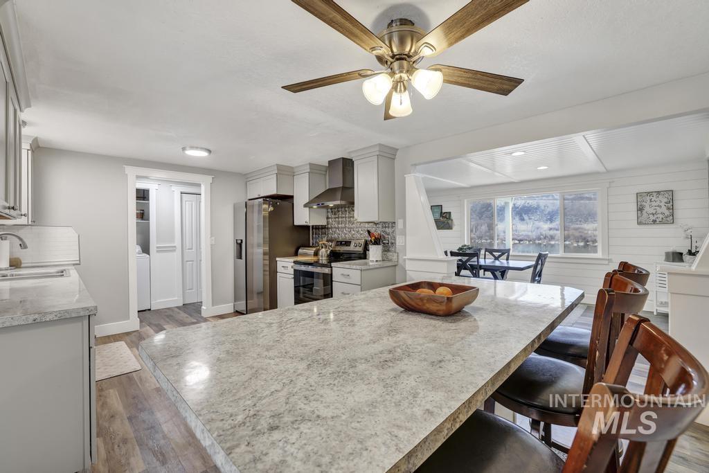 Kitchen featuring stainless steel electric stove, light wood finished floors, wall chimney exhaust hood, and a breakfast bar area