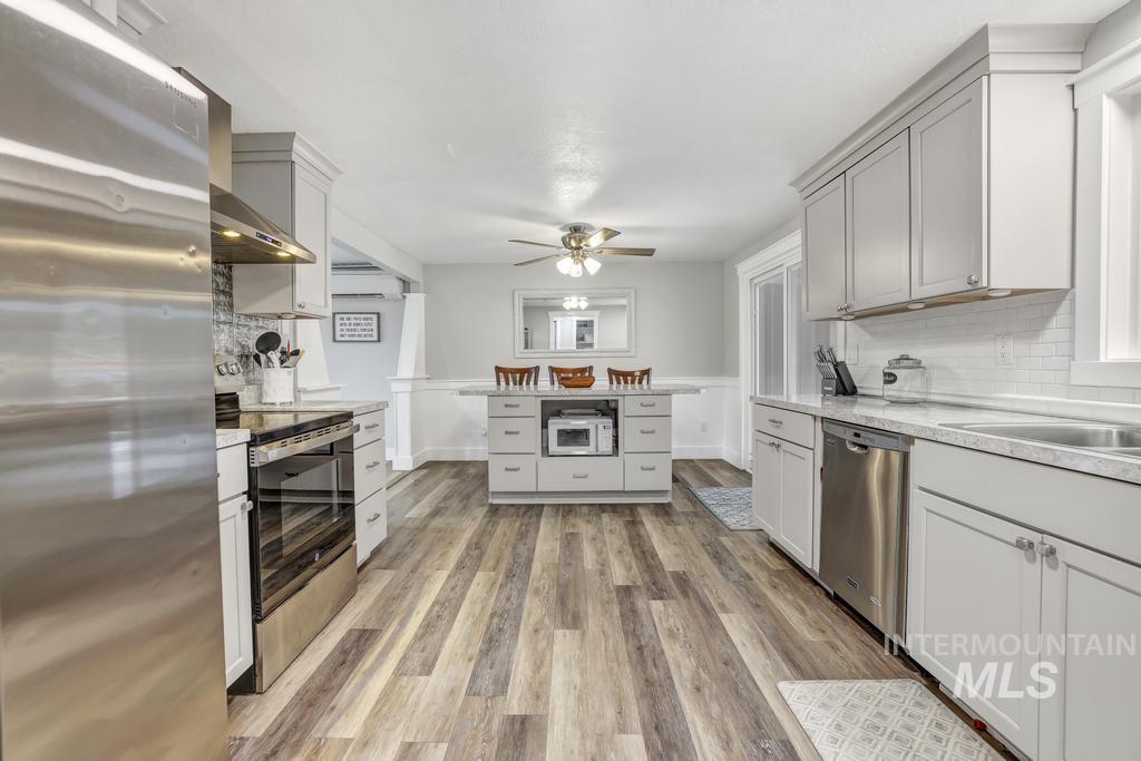 Kitchen with appliances with stainless steel finishes, tasteful backsplash, wall chimney exhaust hood, light wood-style flooring, and ceiling fan