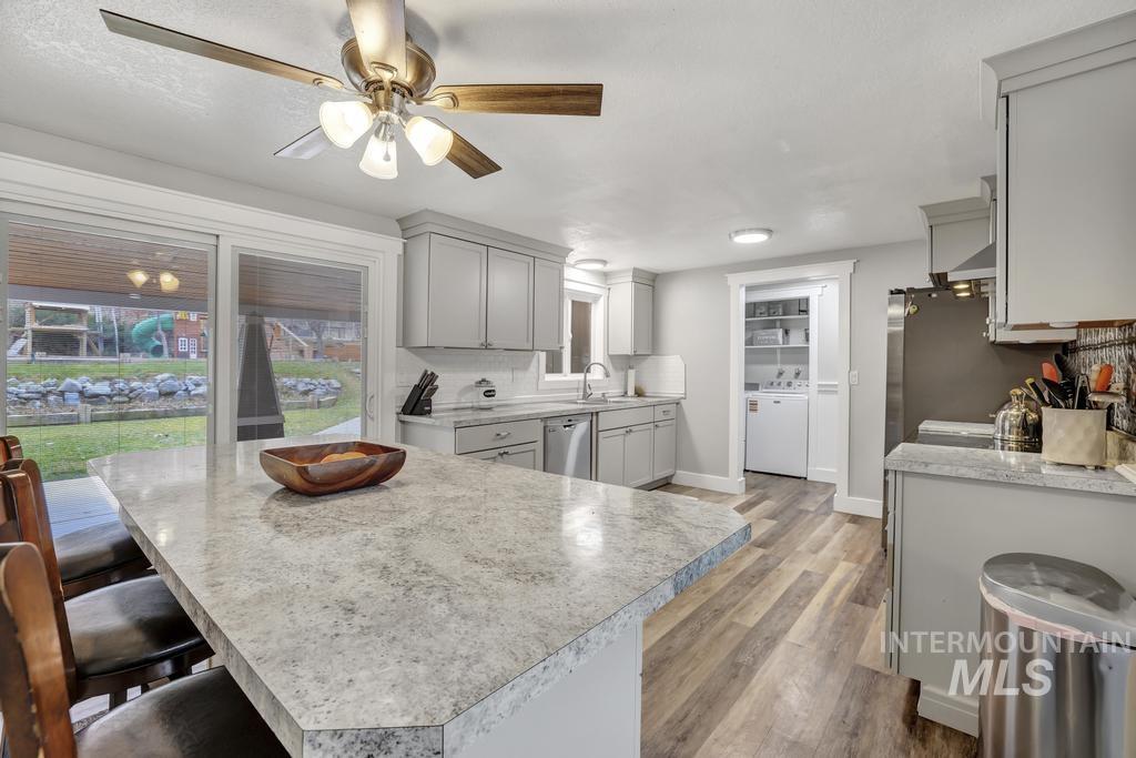 Kitchen with light countertops, gray cabinets, light wood-style flooring, backsplash, and a kitchen breakfast bar