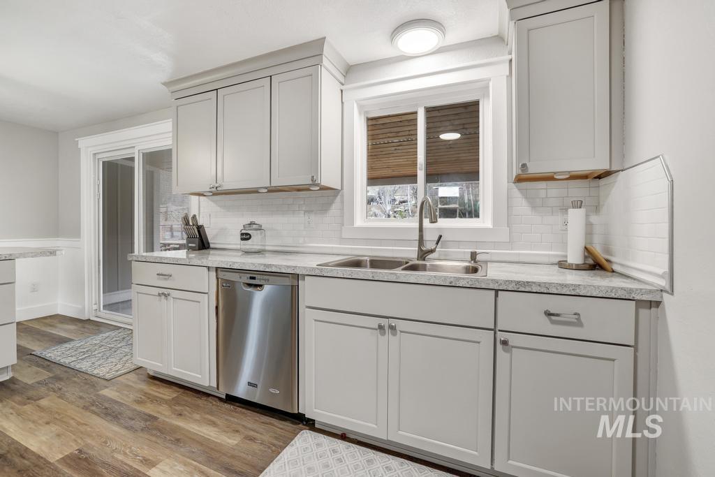 Kitchen with light countertops, stainless steel dishwasher, light wood finished floors, decorative backsplash, and a wainscoted wall