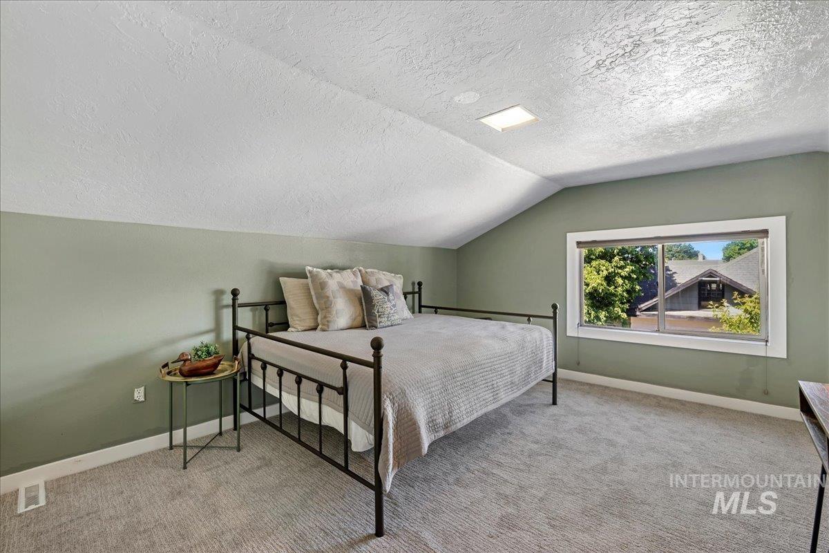 Carpeted bedroom with a textured ceiling and vaulted ceiling