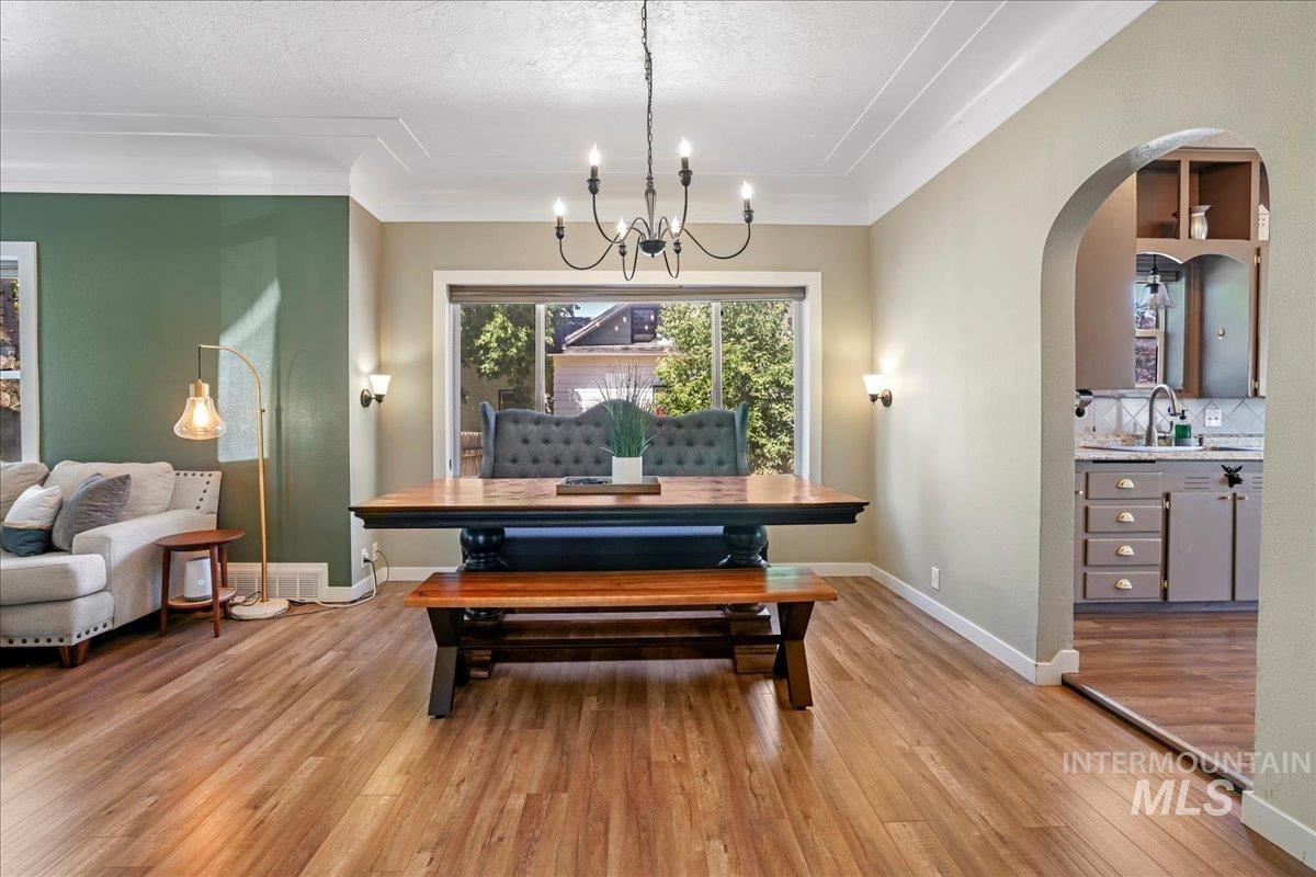 Dining area featuring arched walkways, a chandelier, light wood finished floors, and a textured ceiling