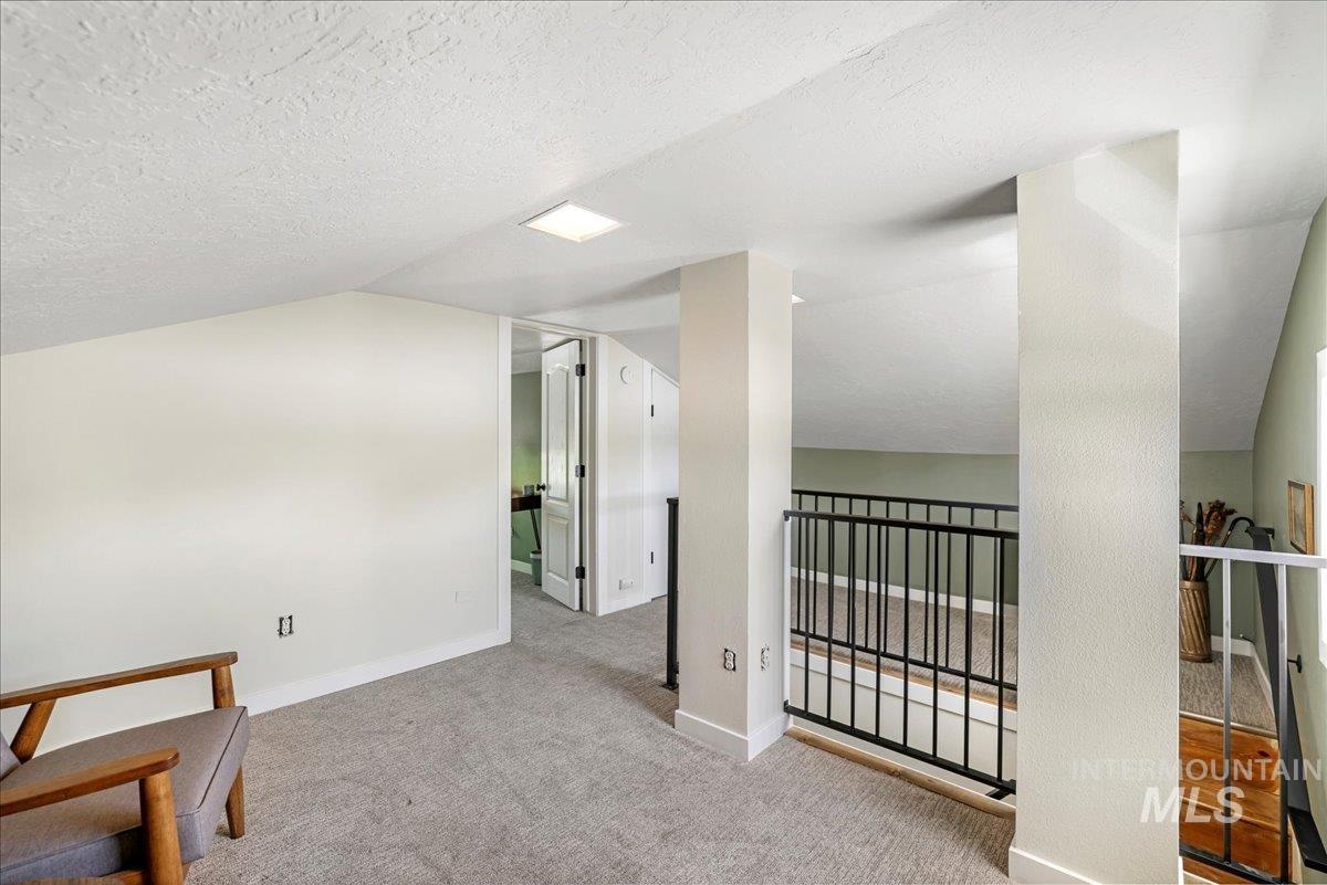 Interior space with vaulted ceiling, carpet flooring, an upstairs landing, and a textured ceiling
