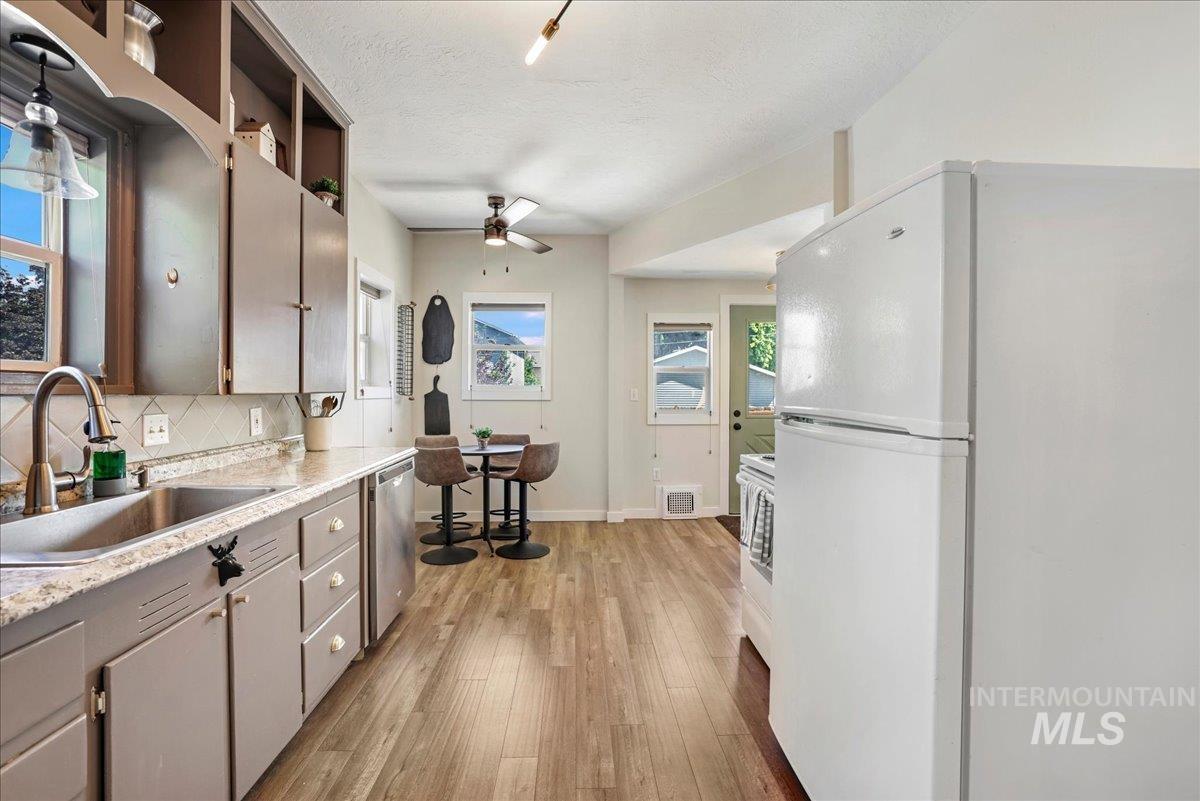 Kitchen with freestanding refrigerator, ceiling fan, dishwasher, light wood finished floors, and light countertops