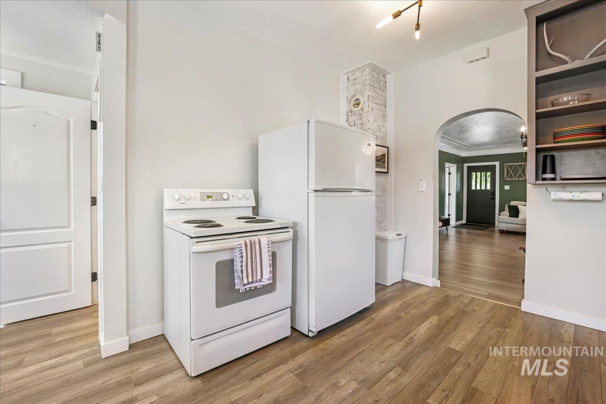 Kitchen with white appliances, arched walkways, light wood-style floors, crown molding, and open shelves