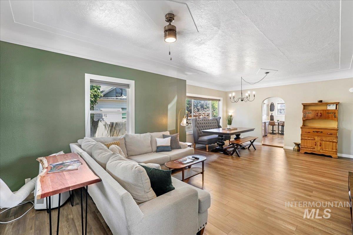 Living room with a textured ceiling, ceiling fan, arched walkways, light wood finished floors, and a chandelier