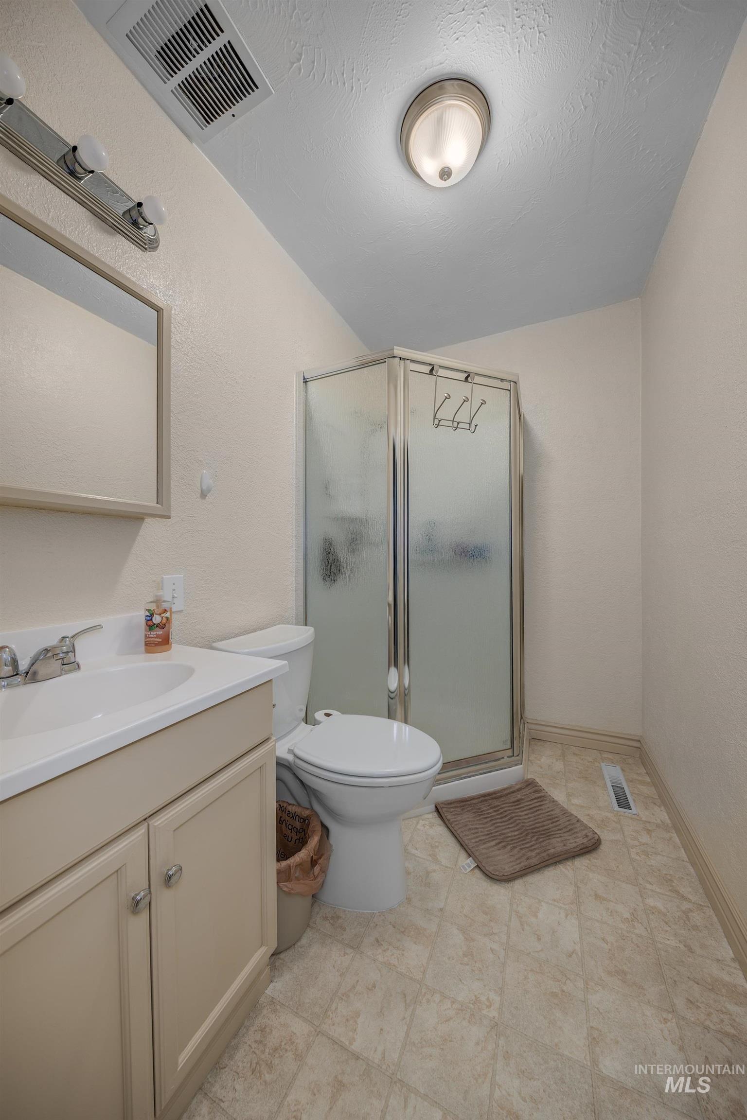 Bathroom featuring a shower stall, vanity, a textured wall, and lofted ceiling