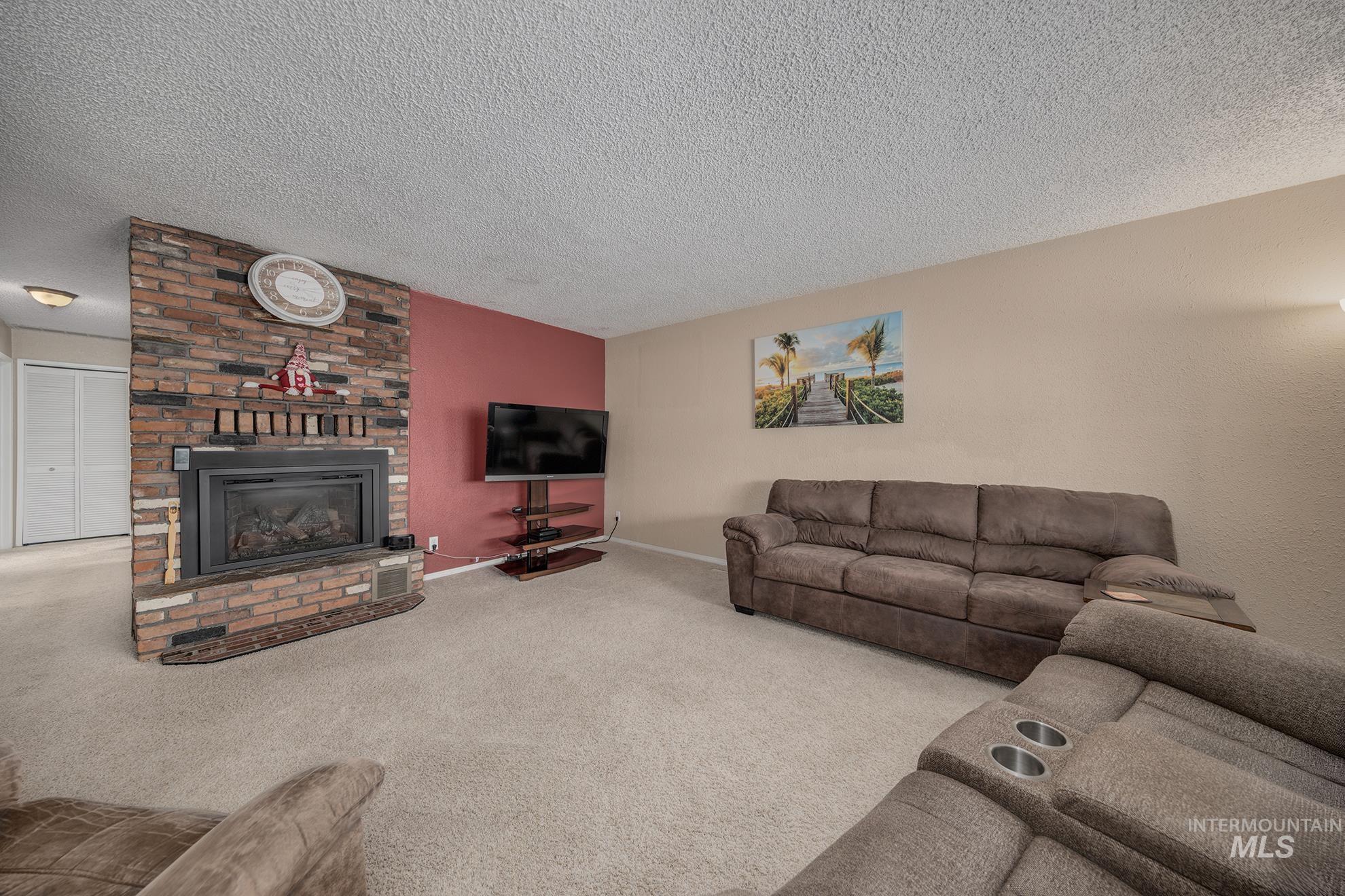 Living room featuring carpet floors, a brick fireplace, and a textured ceiling