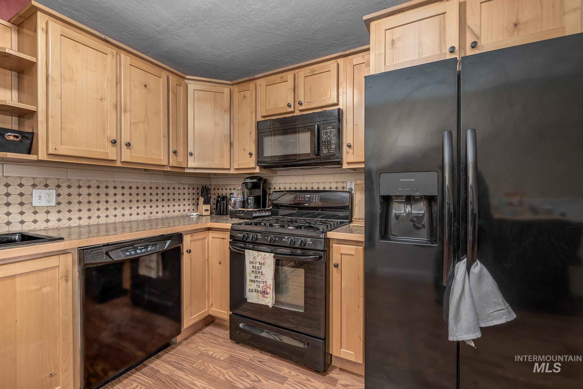 Kitchen featuring black appliances, open shelves, light wood finish cabinetry, light wood finished floors, and decorative backsplash