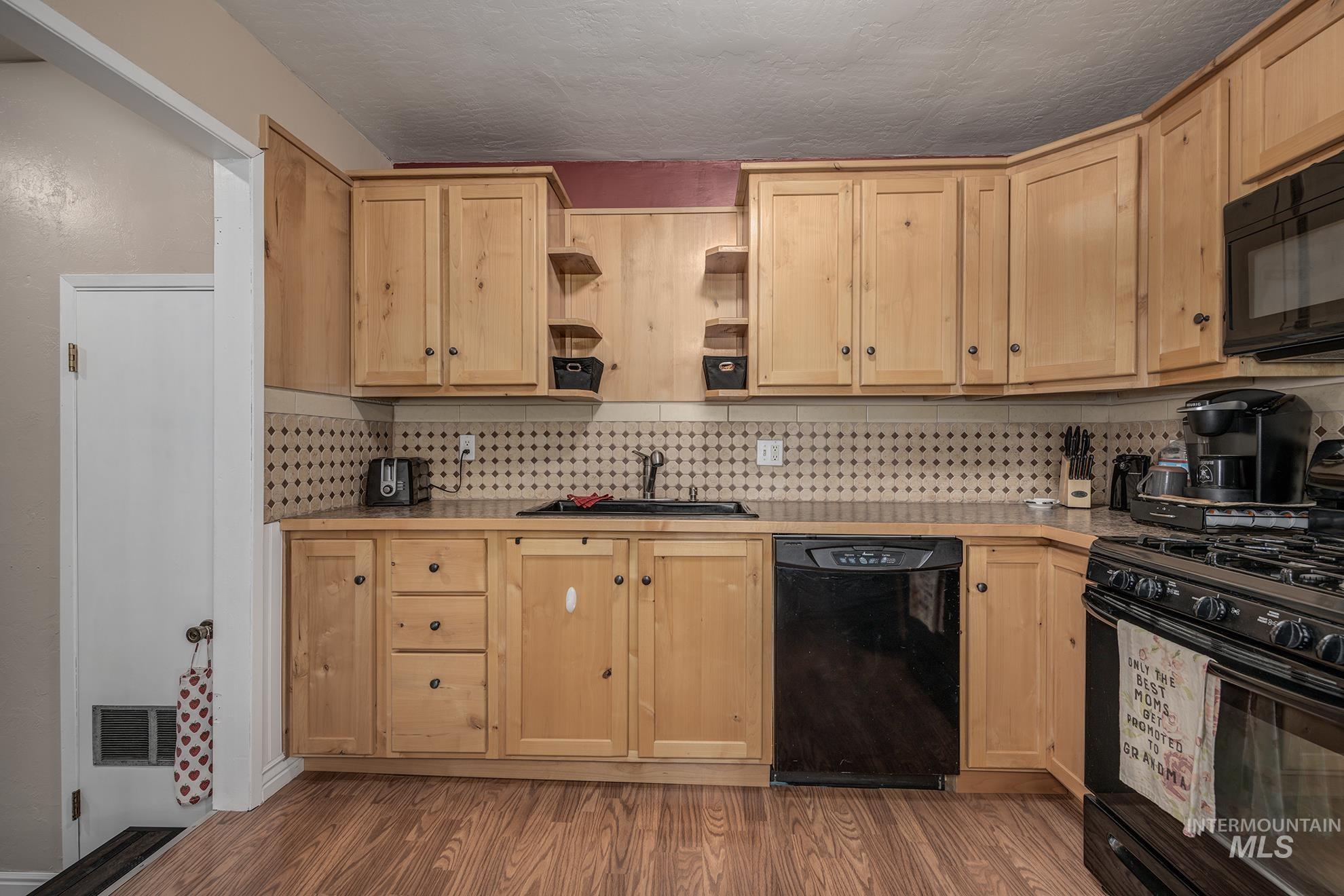 Kitchen featuring black appliances, light wood finish cabinetry, backsplash, light wood-style flooring, and open shelves