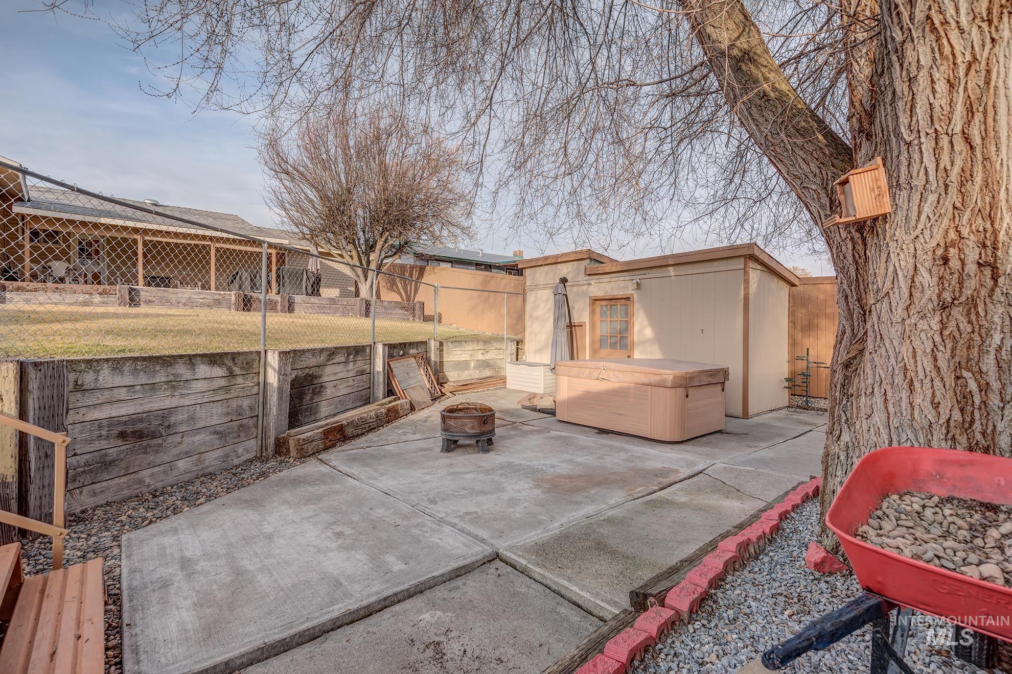 Fenced backyard featuring a hot tub, an outdoor structure, a patio area, and a fire pit