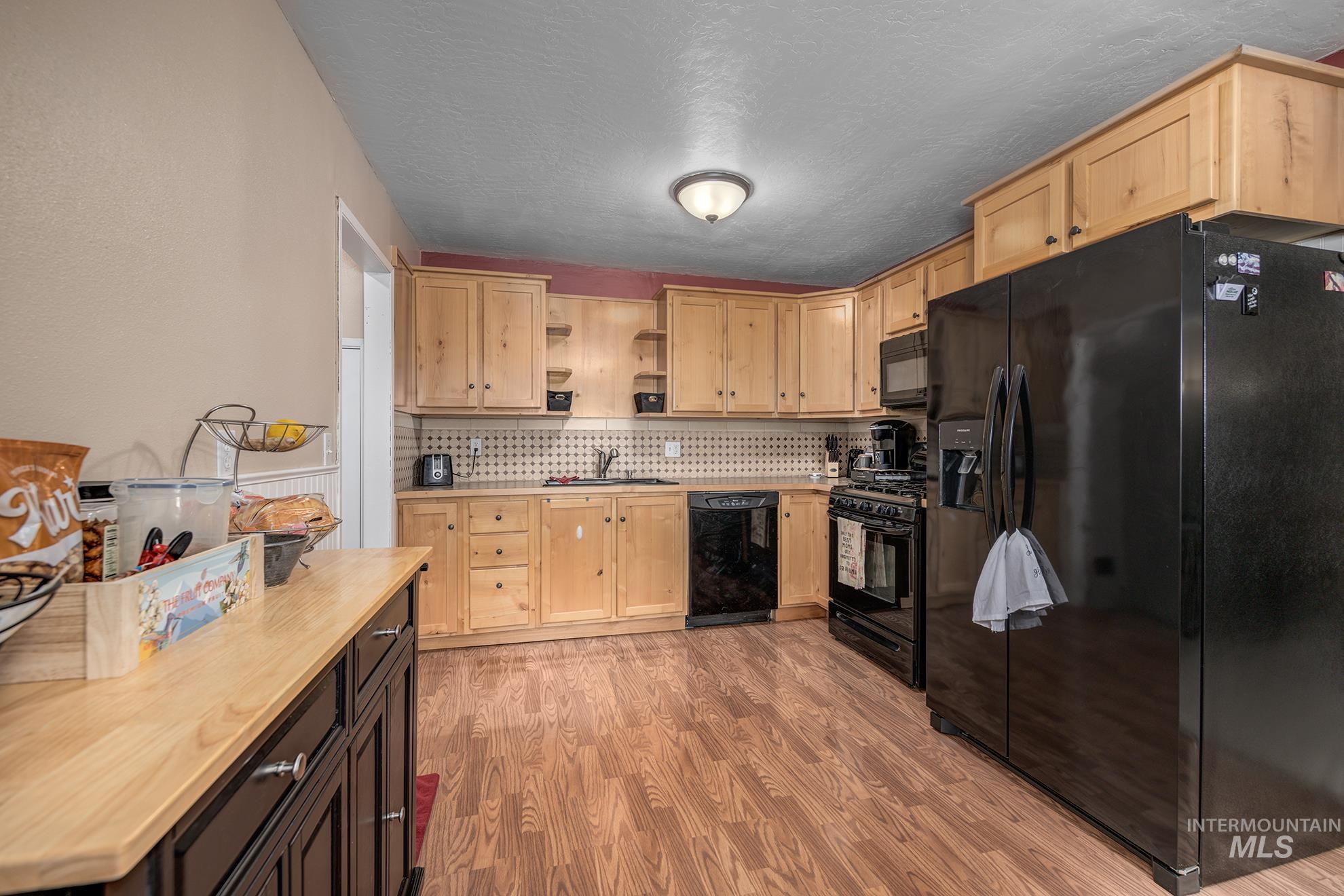 Kitchen with black appliances, open shelves, light wood finish cabinetry, light wood-type flooring, and tasteful backsplash