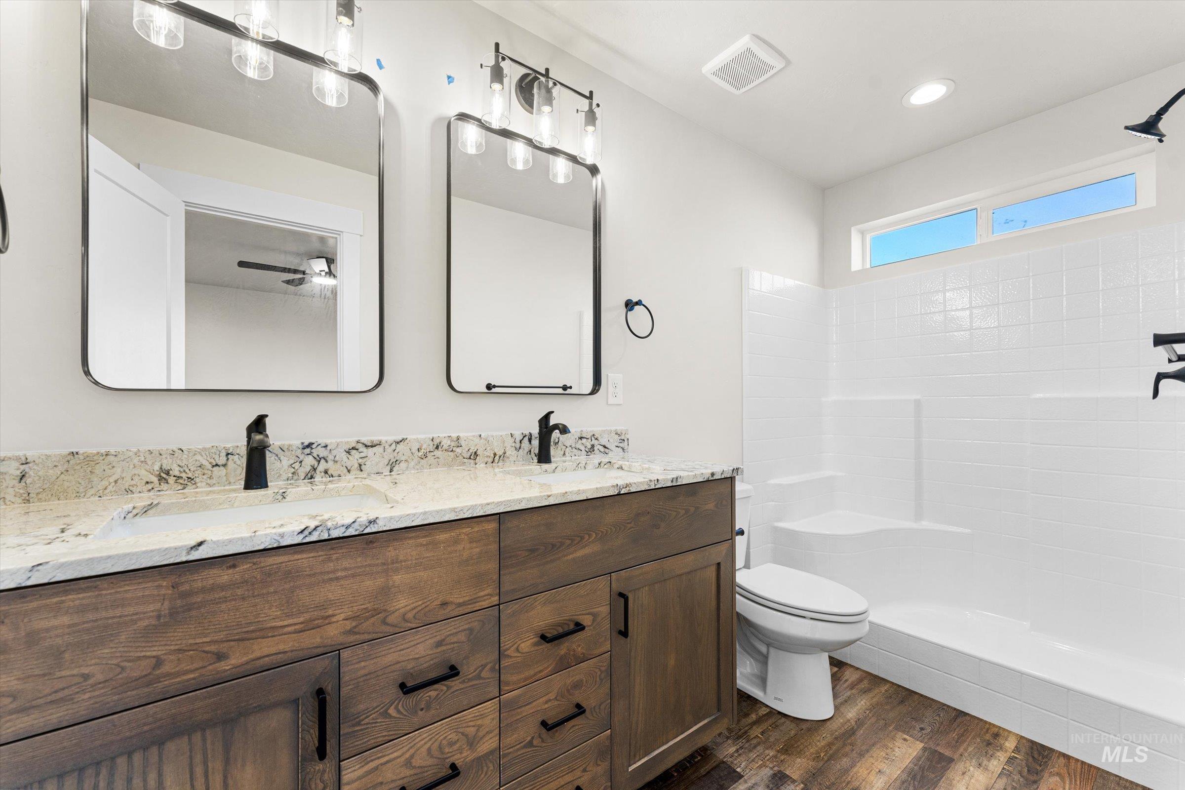 Bathroom with double vanity, a tile shower, and dark wood-type flooring