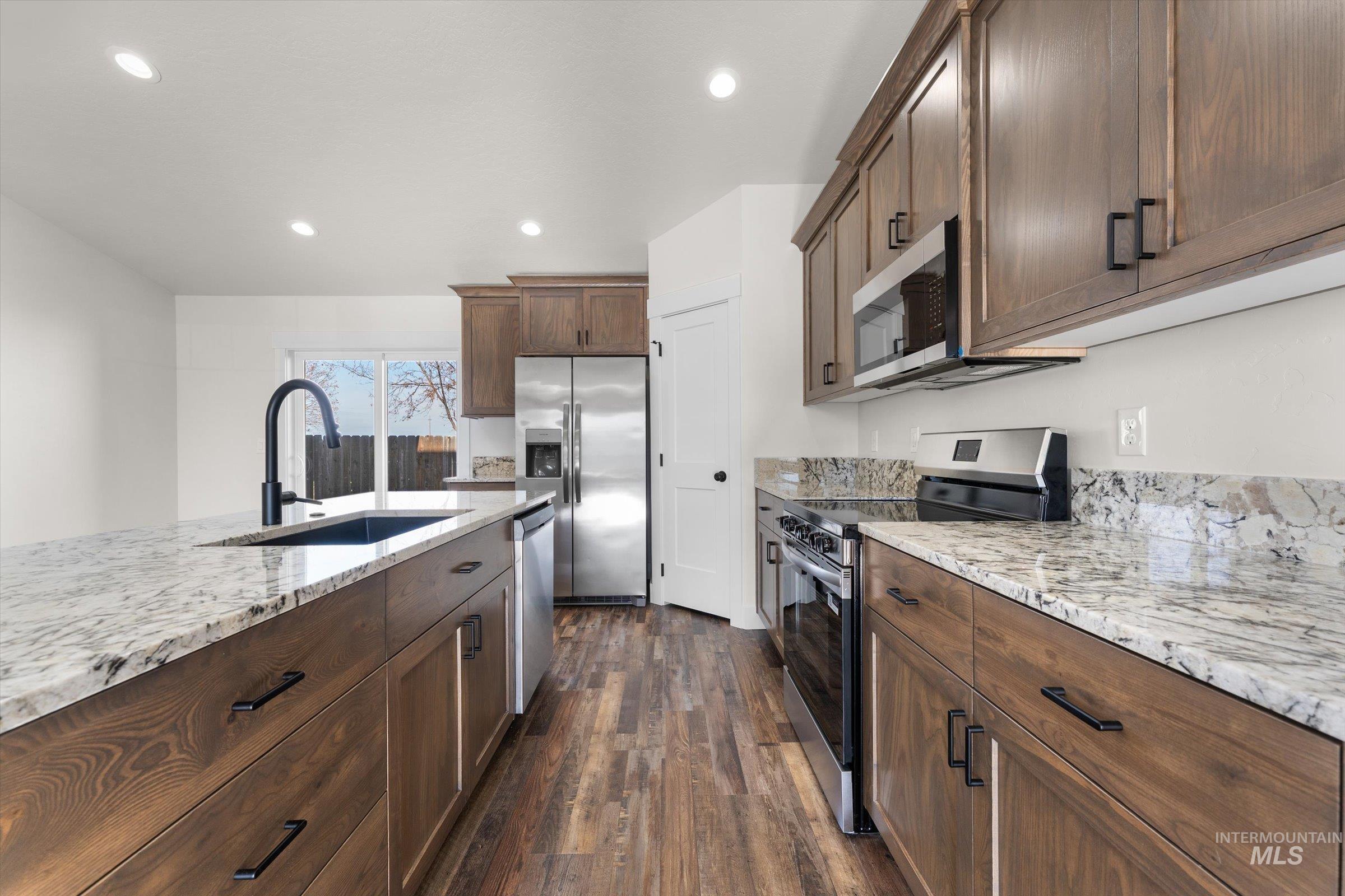 Kitchen featuring appliances with stainless steel finishes, dark wood-style floors, light stone countertops, recessed lighting, and dark brown cabinetry