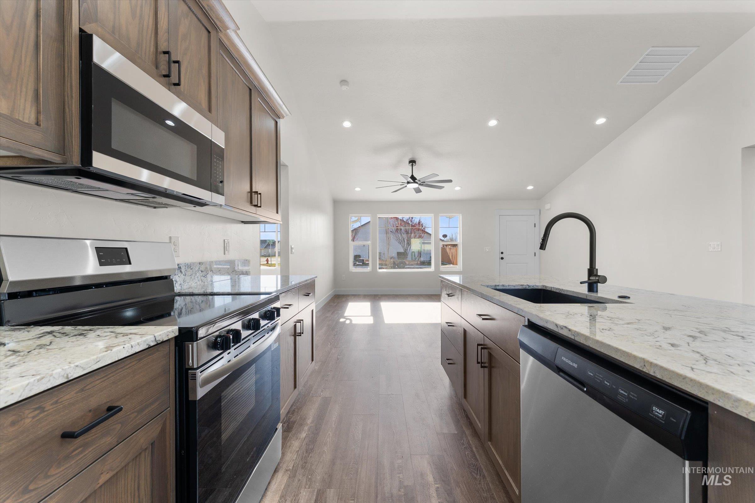 Kitchen featuring stainless steel appliances, light stone countertops, dark wood-type flooring, a ceiling fan, and dark brown cabinets