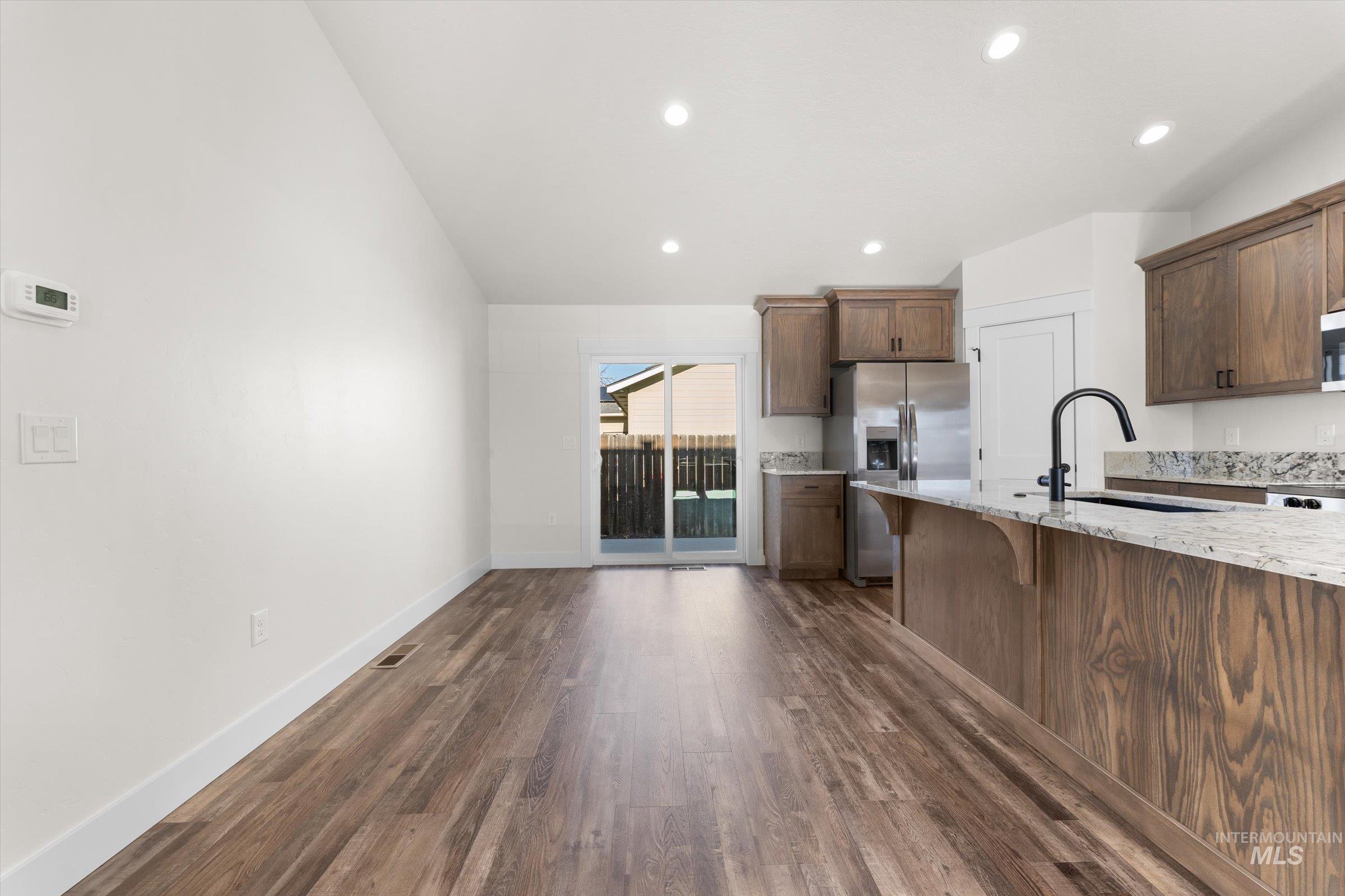 Kitchen featuring stainless steel refrigerator with ice dispenser, light stone countertops, dark wood finished floors, lofted ceiling, and a breakfast bar area