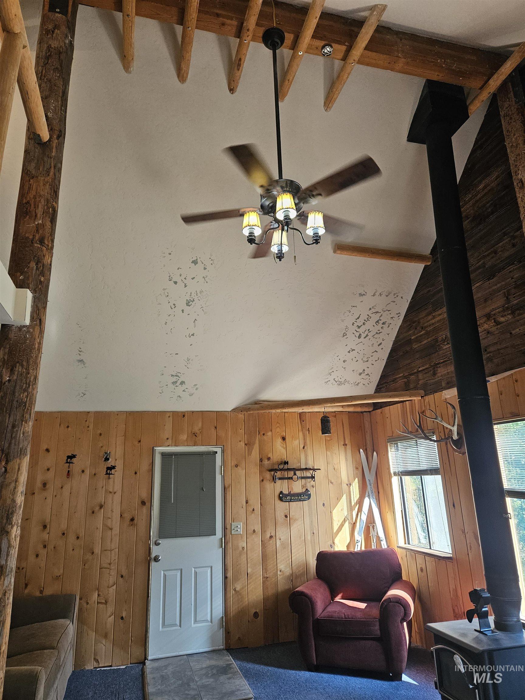 Living room with high vaulted ceiling, a wood stove, and wooden walls