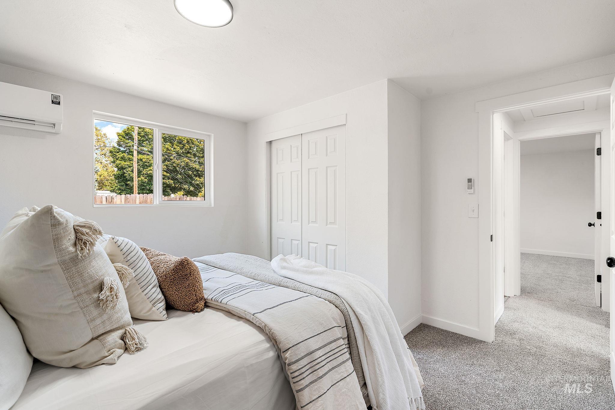 Bedroom with light carpet, a closet, and a wall mounted air conditioner