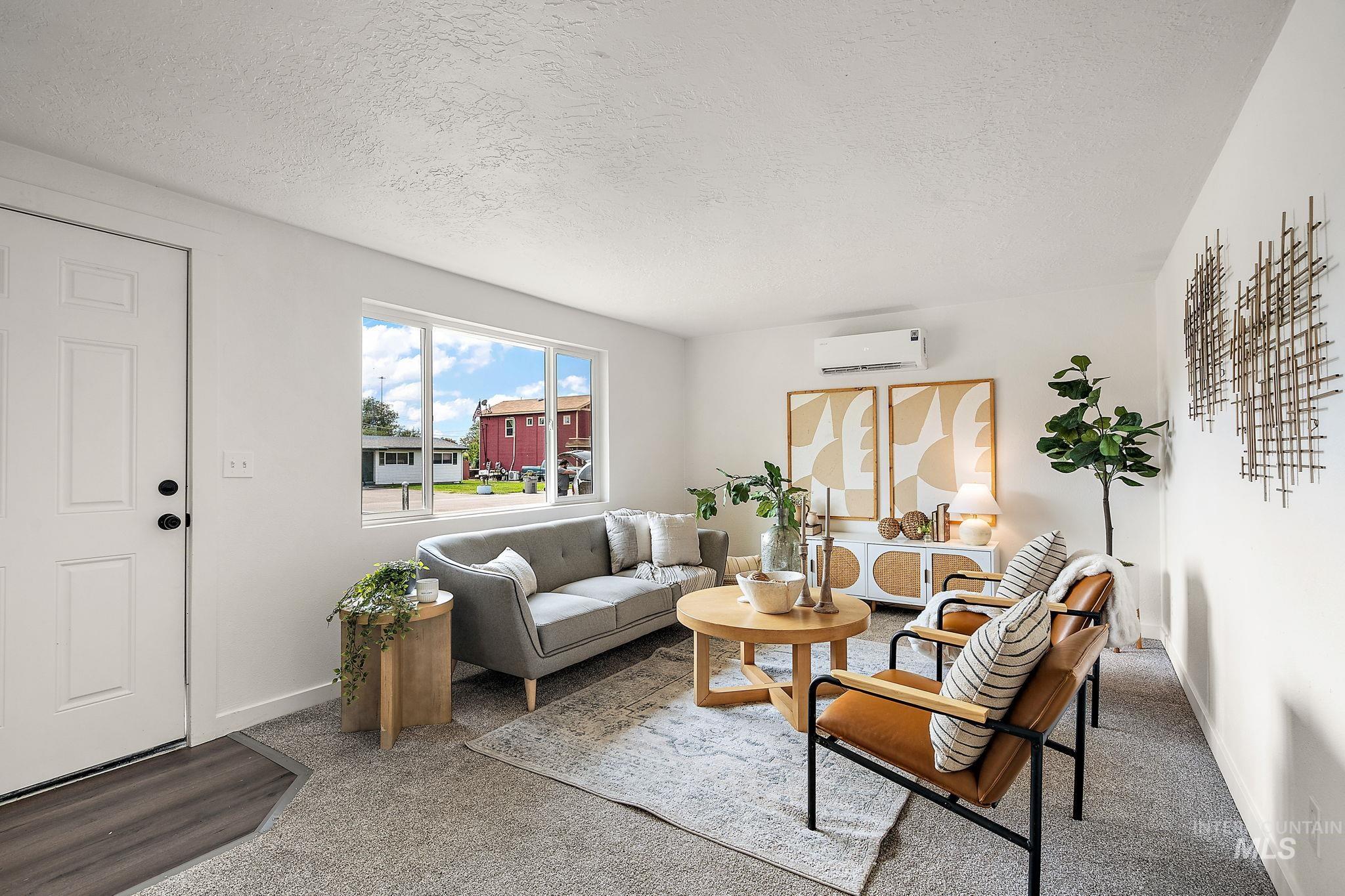 Living area with carpet flooring, a textured ceiling, and a wall mounted AC