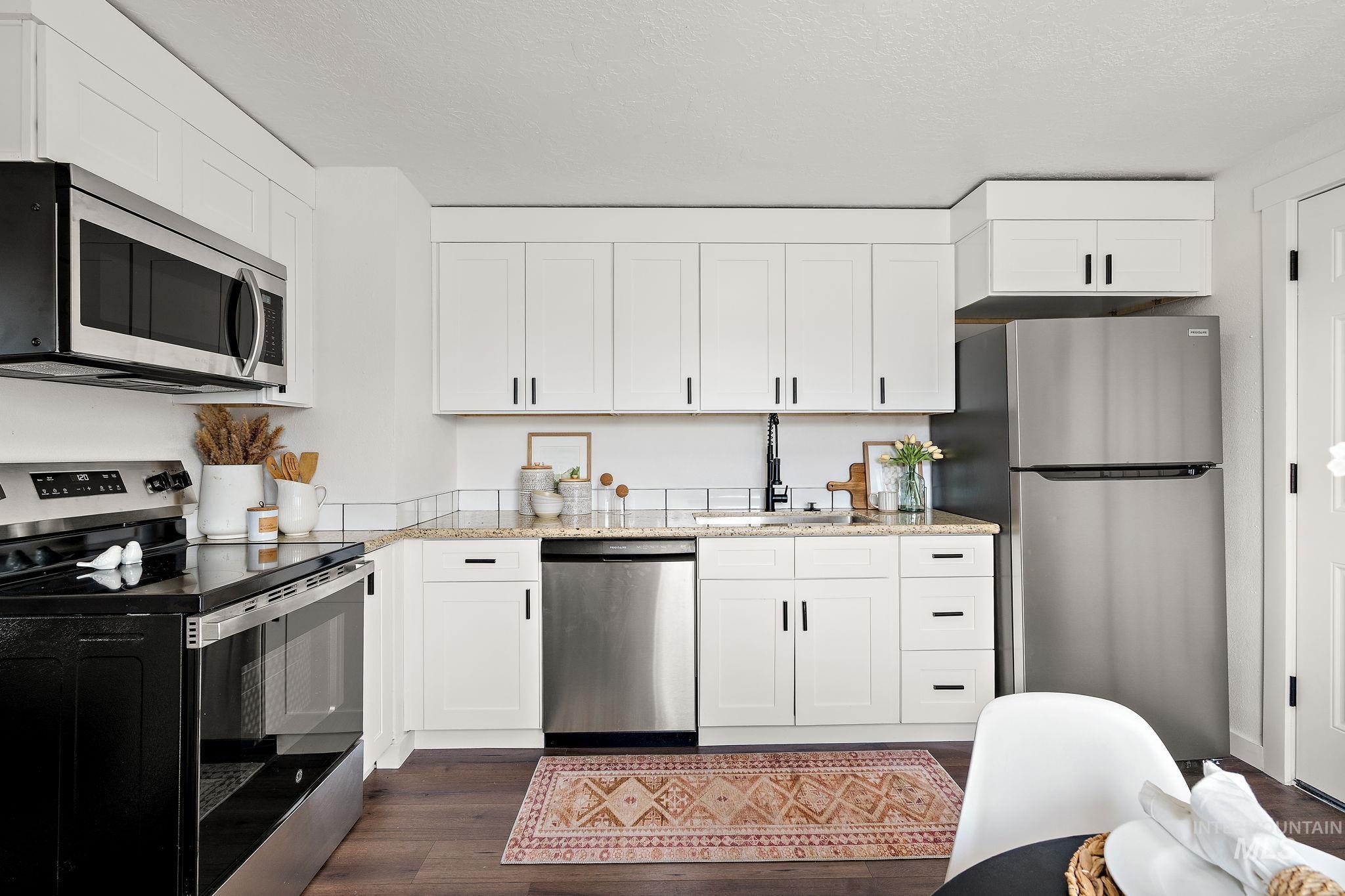 Kitchen featuring stainless steel appliances, light stone countertops, dark wood-style flooring, and white cabinets