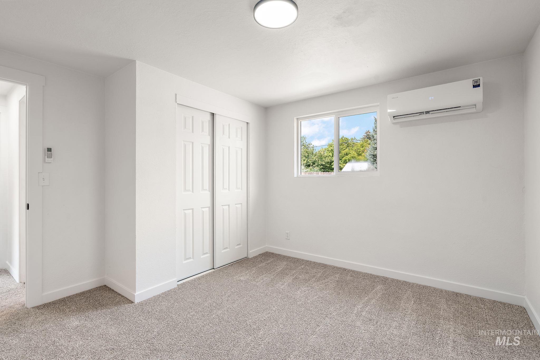 Unfurnished bedroom featuring light colored carpet, a wall mounted AC, and a closet