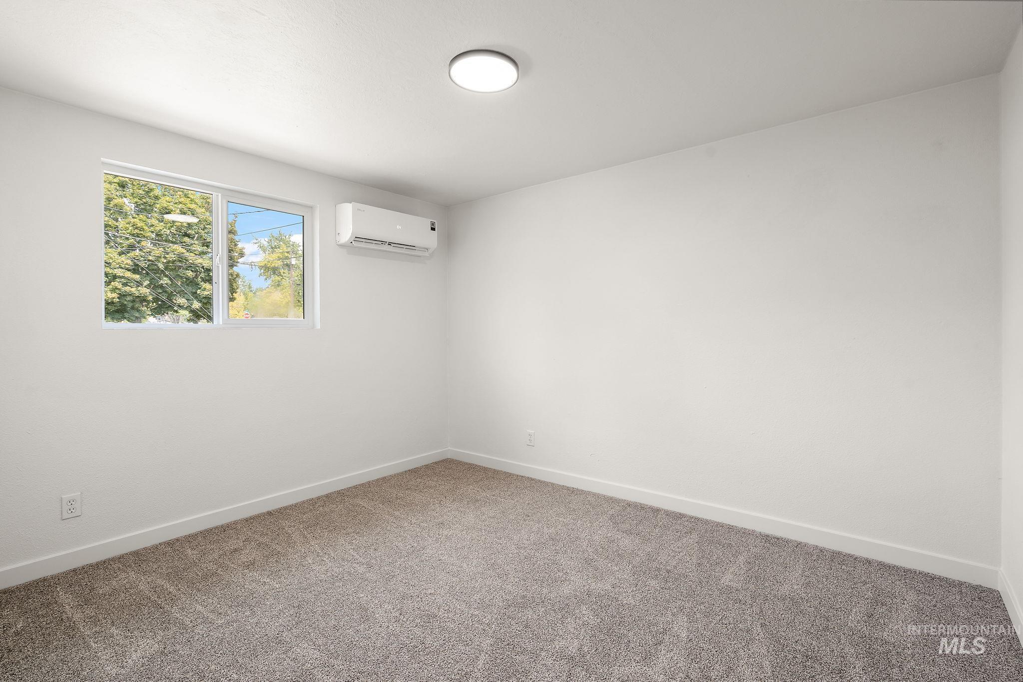 Carpeted spare room with baseboards and an AC wall unit