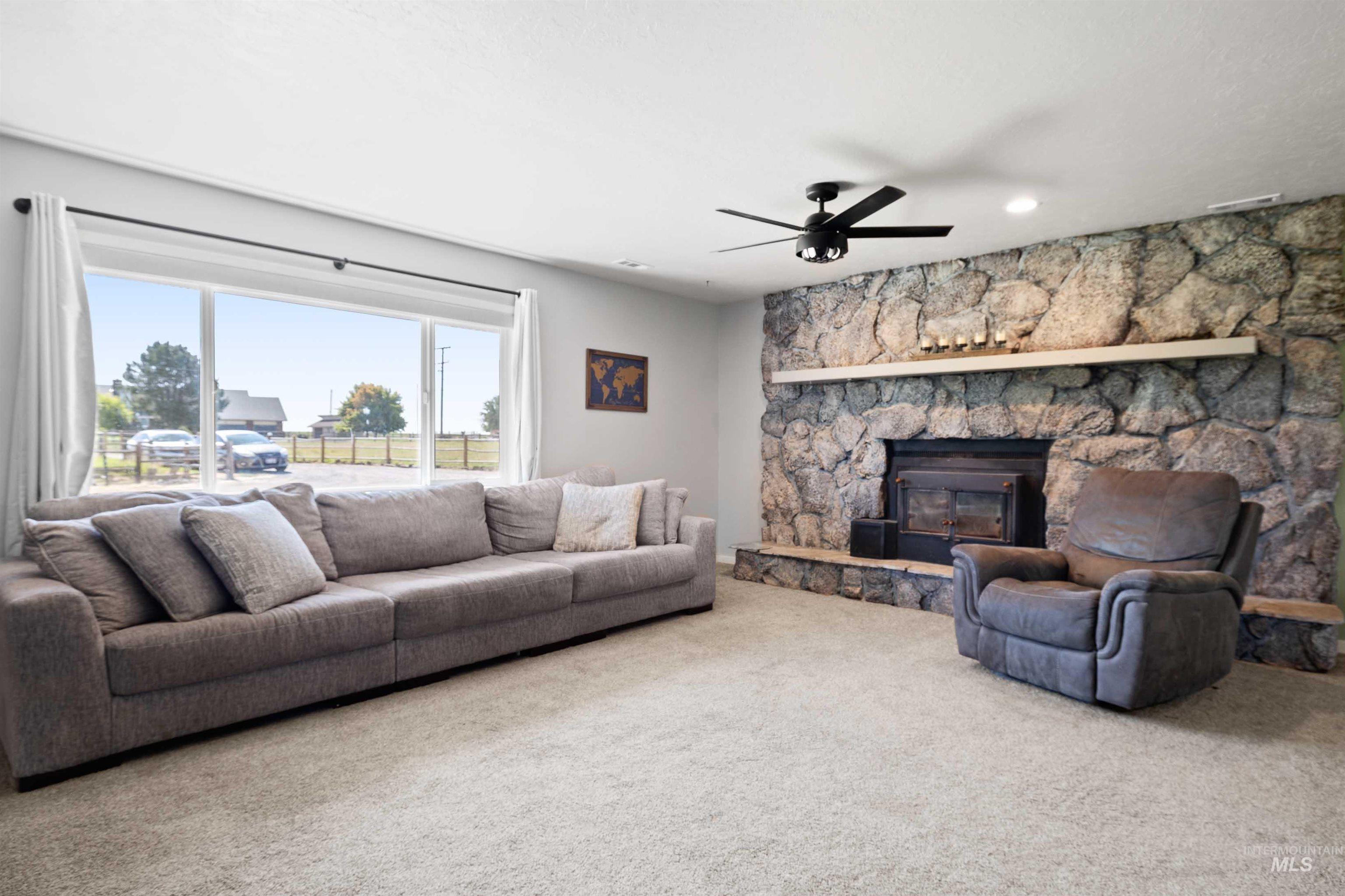 Carpeted living room featuring ceiling fan and a stone fireplace