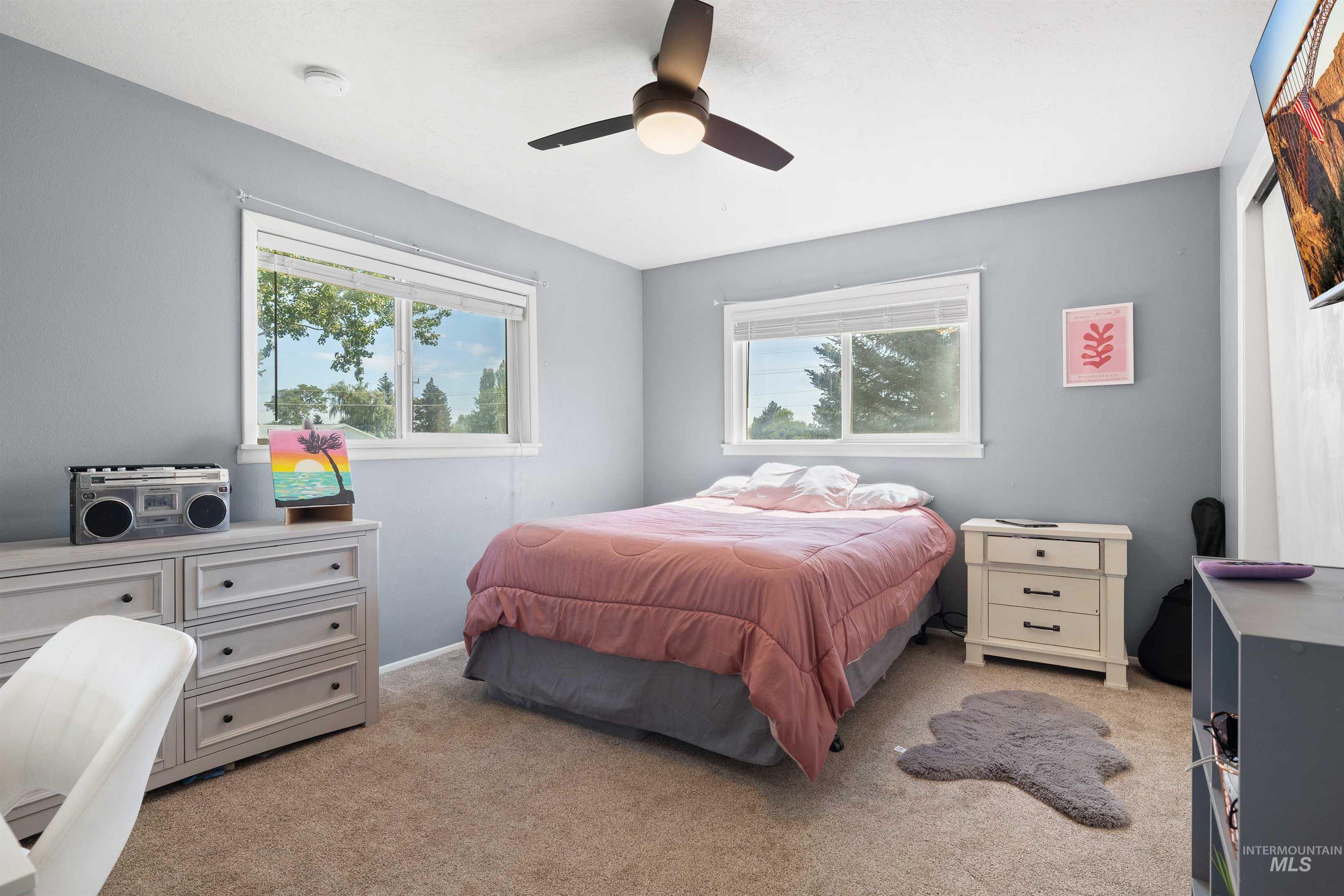 Bedroom with multiple windows, light colored carpet, and ceiling fan