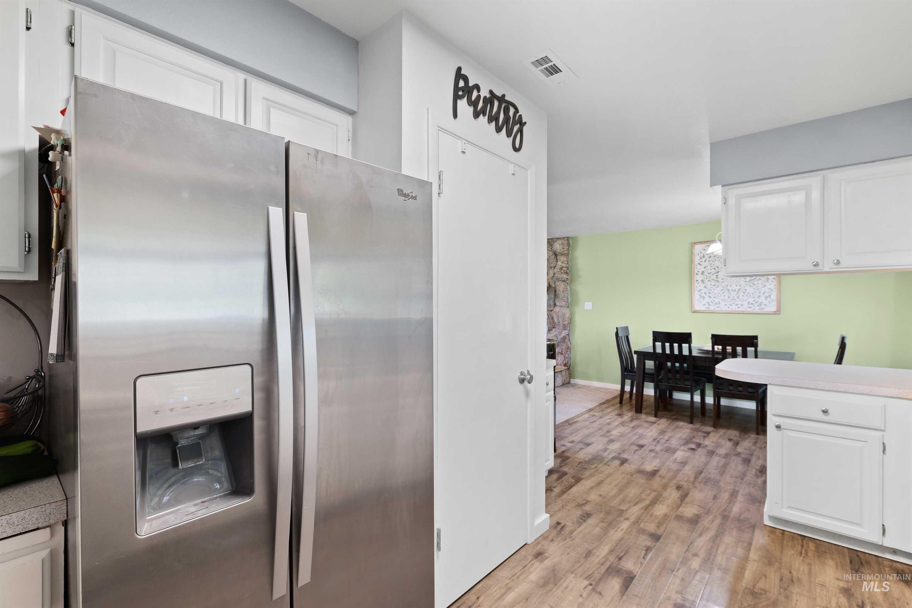 Kitchen featuring stainless steel fridge, white cabinets, light wood-style floors, and light countertops
